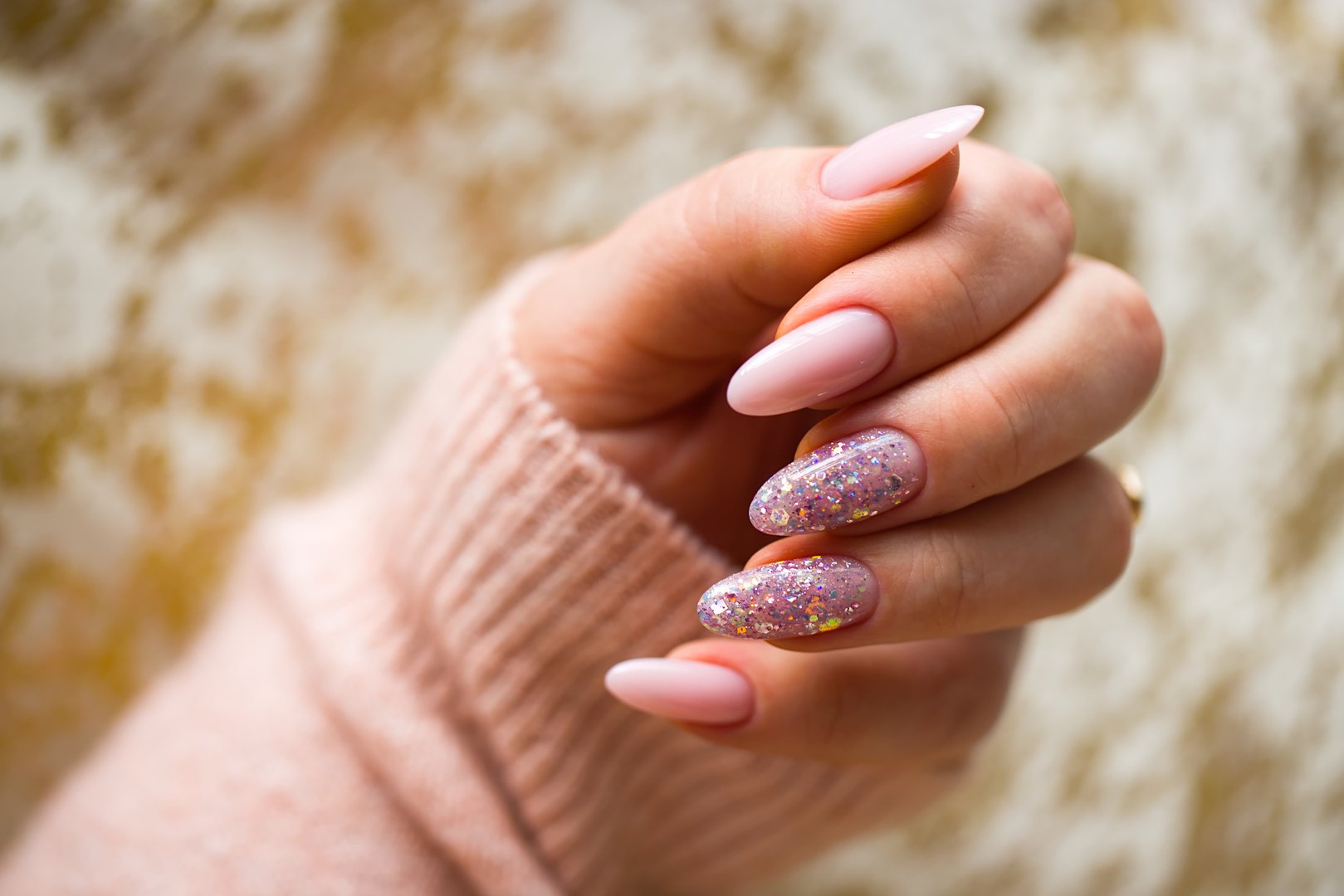 An image featuring a woman's hand with stunning pink gel nails, meticulously painted and adorned with stylish multicolored glitter. The hand is well-maintained and nourished.