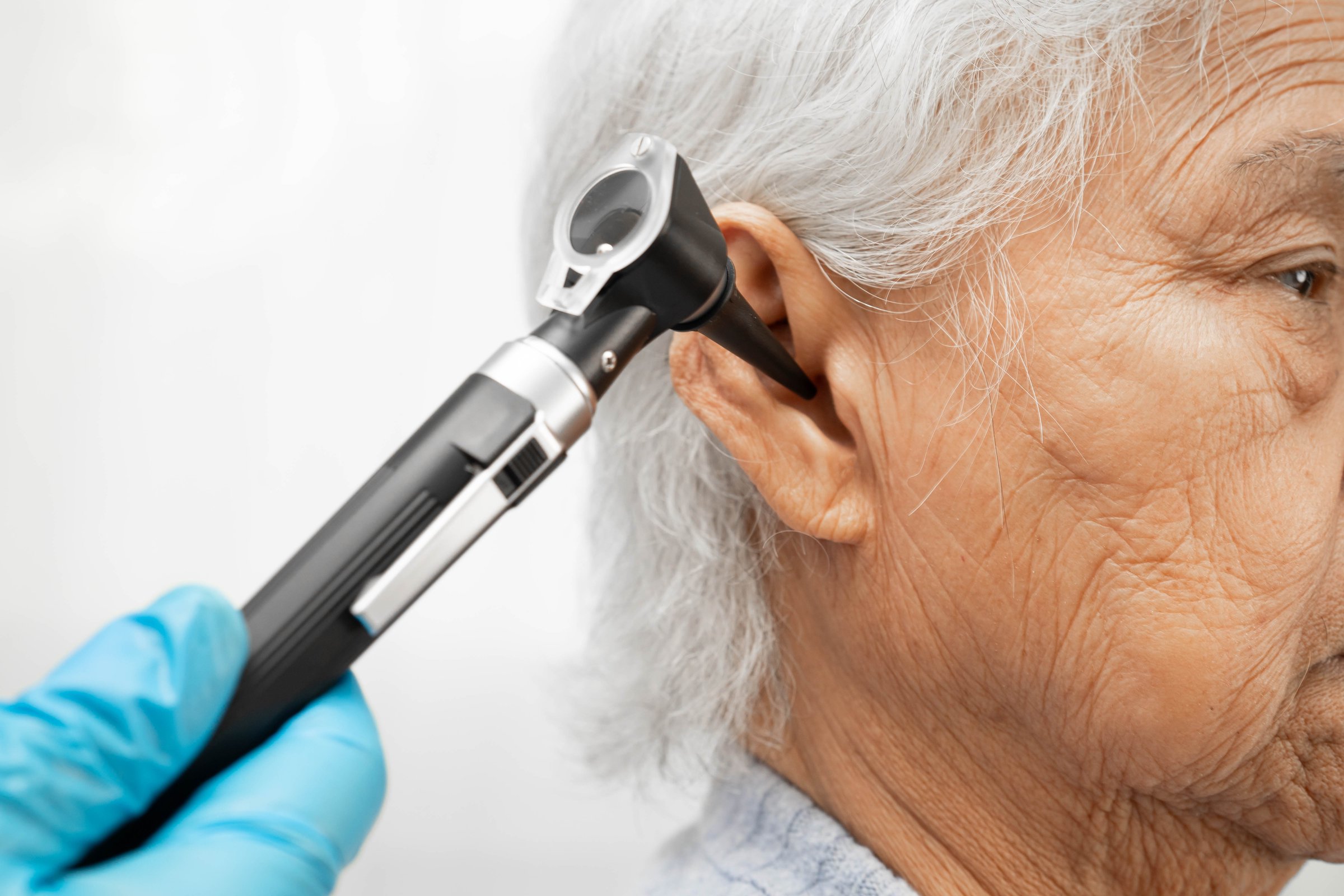 Otolaryngologist or ENT physician doctor examining senior patient ear with otoscope, hearing loss problem.