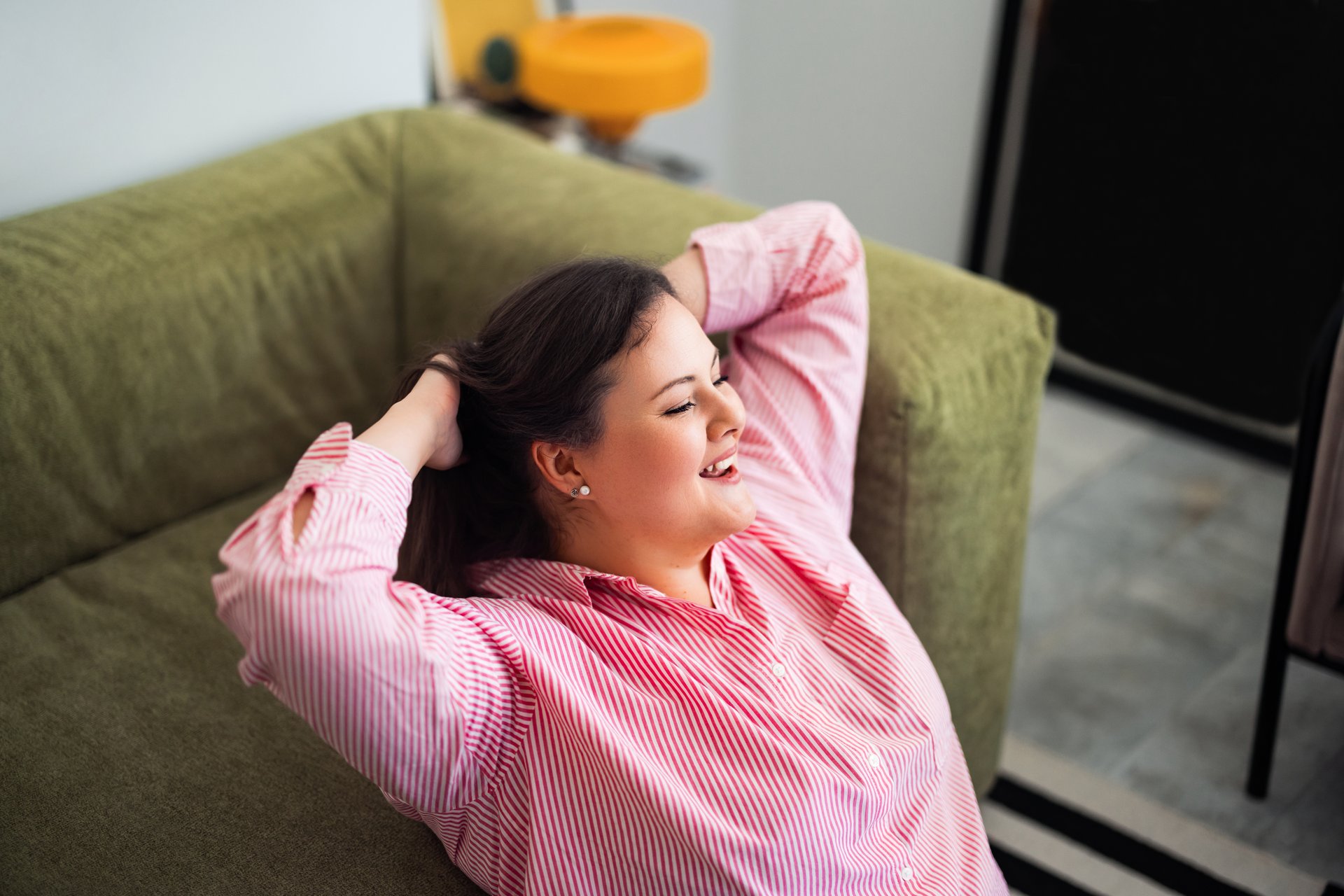 A cheerful individual lounging on a comfortable green sofa, enjoying a casual and carefree moment in a cozy and bright indoor environment, exuding happiness and peace.