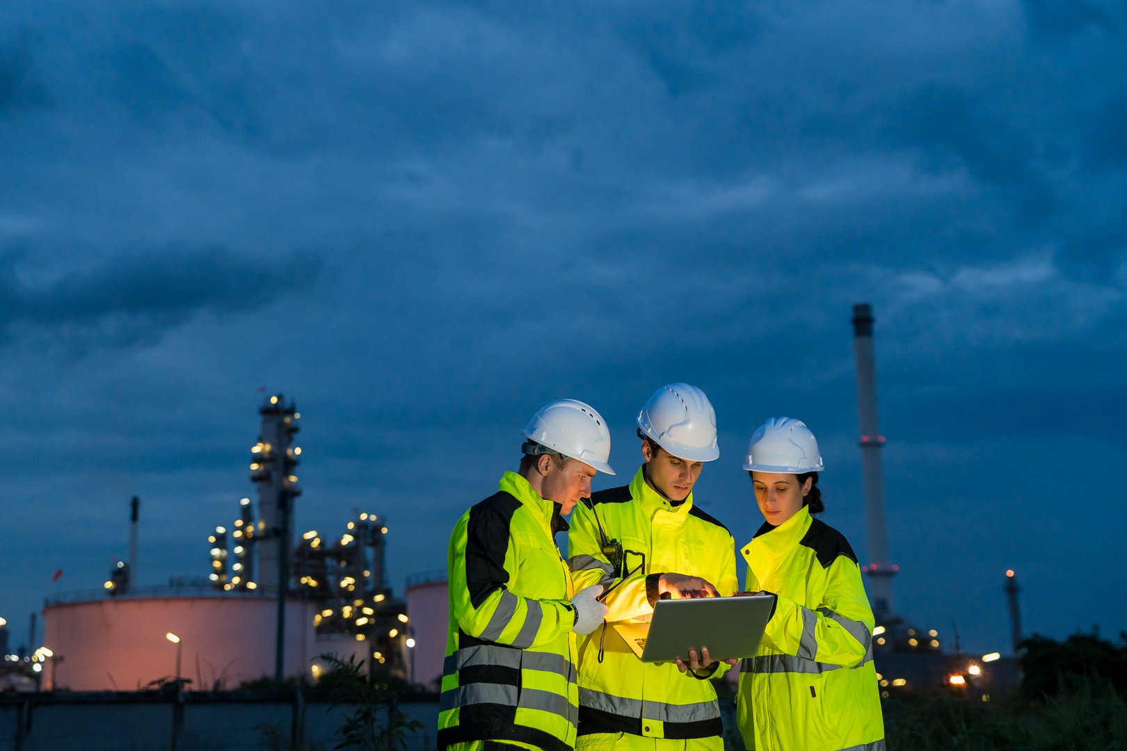 Engineering team collaborating with a laptop during a night shift at a petrochemical refinery.