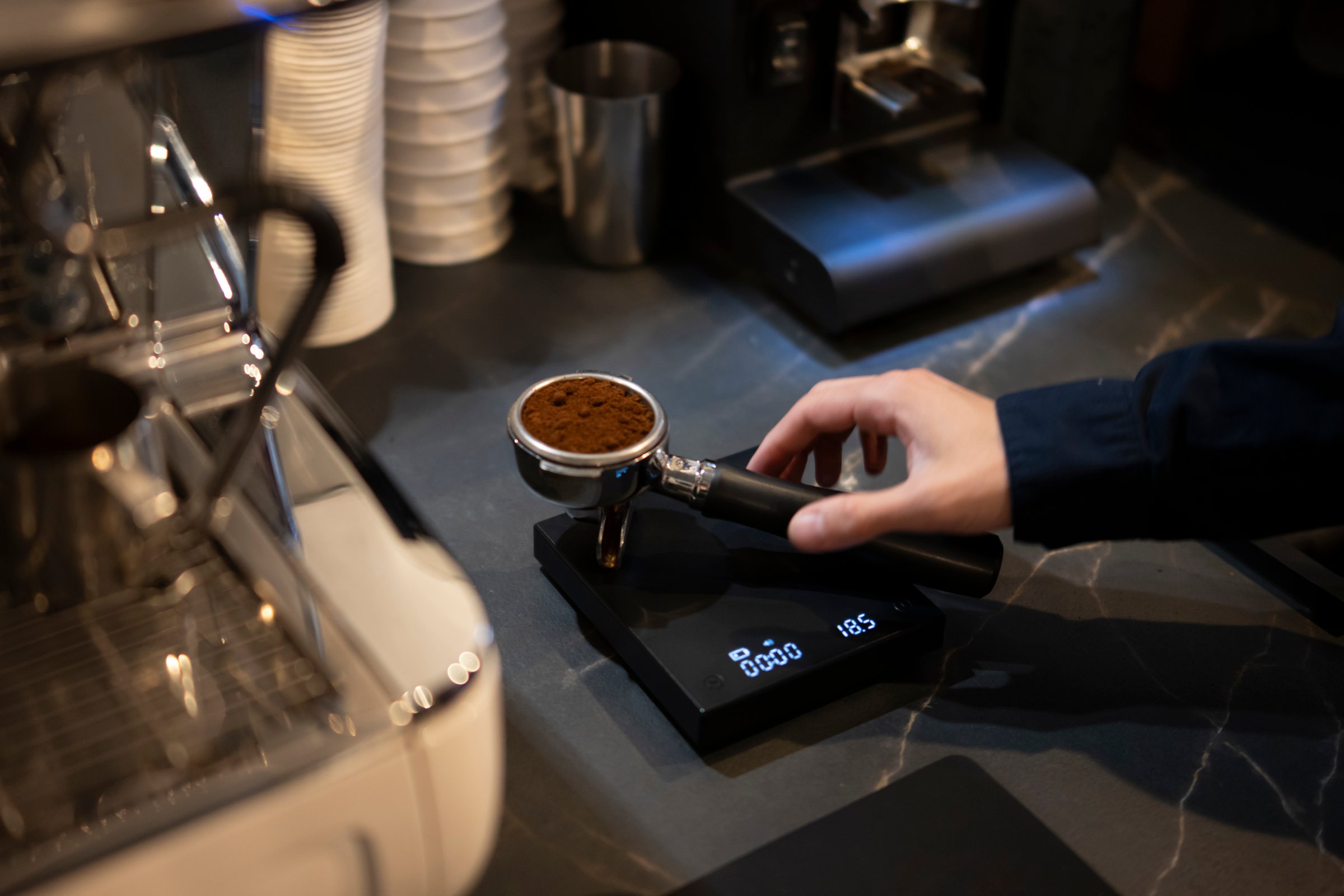 Barista Pressing Ground Coffee Into a Portafilter With a Tamper at a Cafe