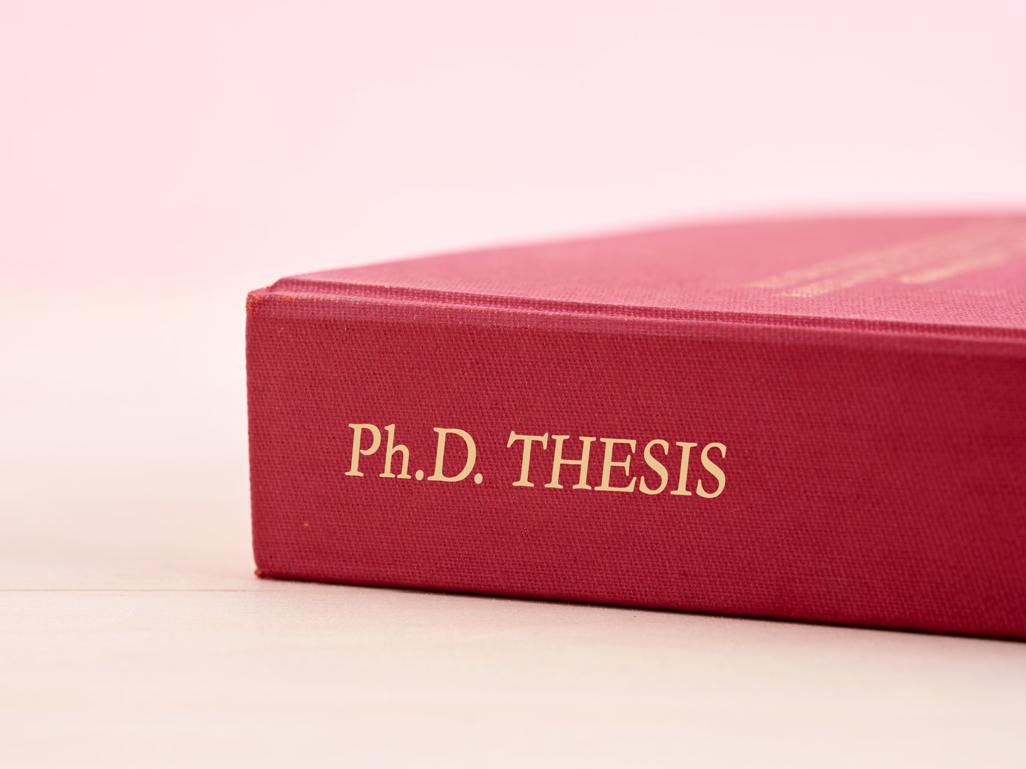 Close-up of a hardcover PhD thesis book with a red cover on a wooden table. PhD thesis and graduation concept.