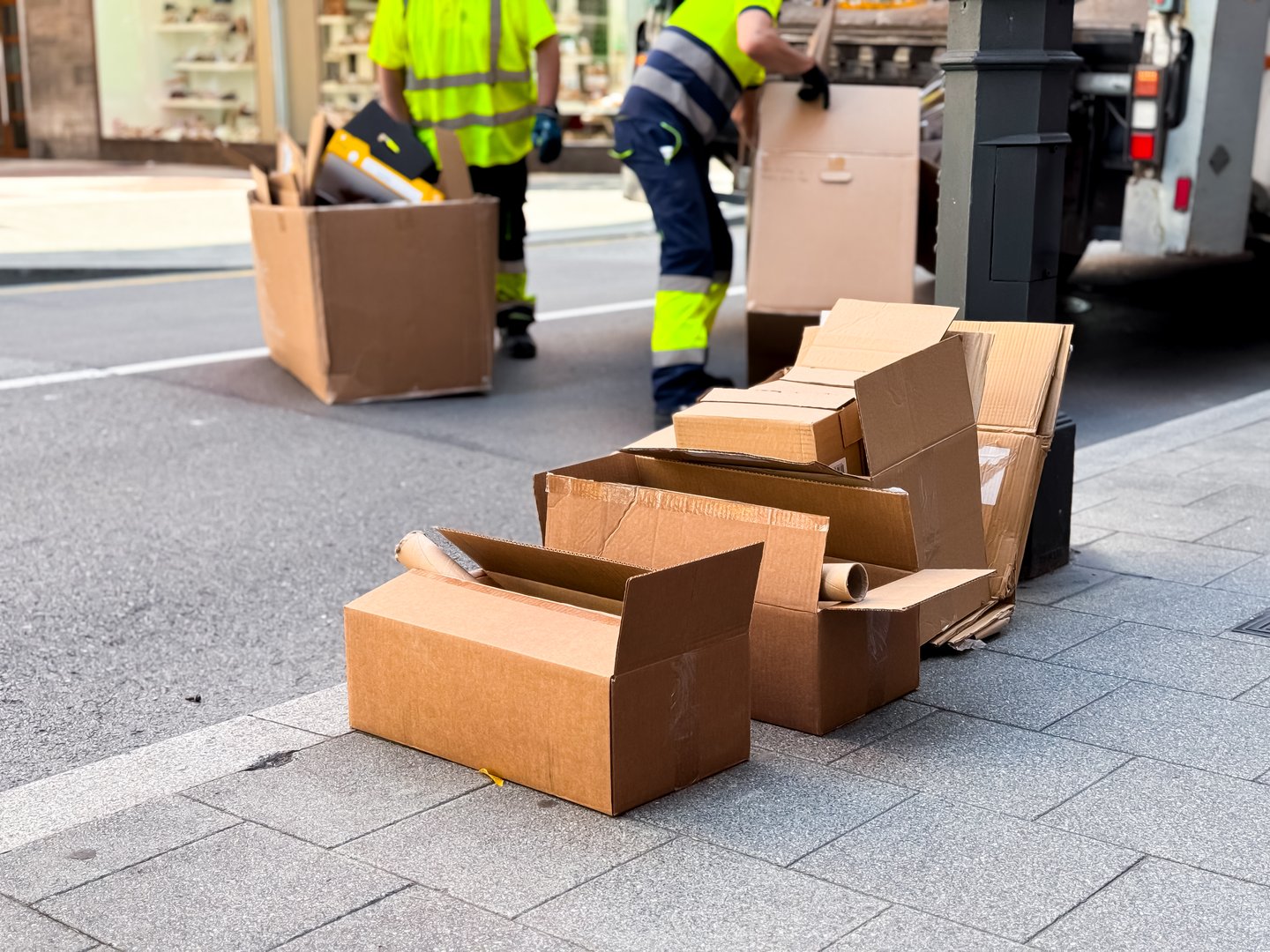 Workers dispose of cardboard boxes on city street sidewalk. High quality.