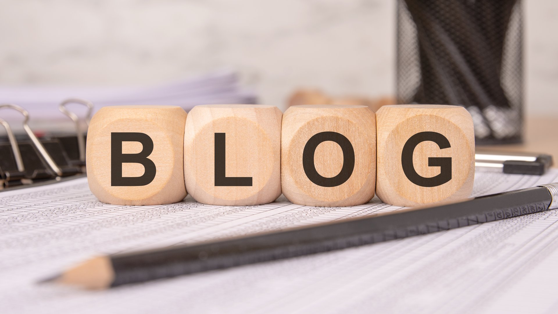 four wooden cubes forming the word BLOG rest on a desk with office supplies, highlighting content creation, writing, and digital communication in a professional workspace