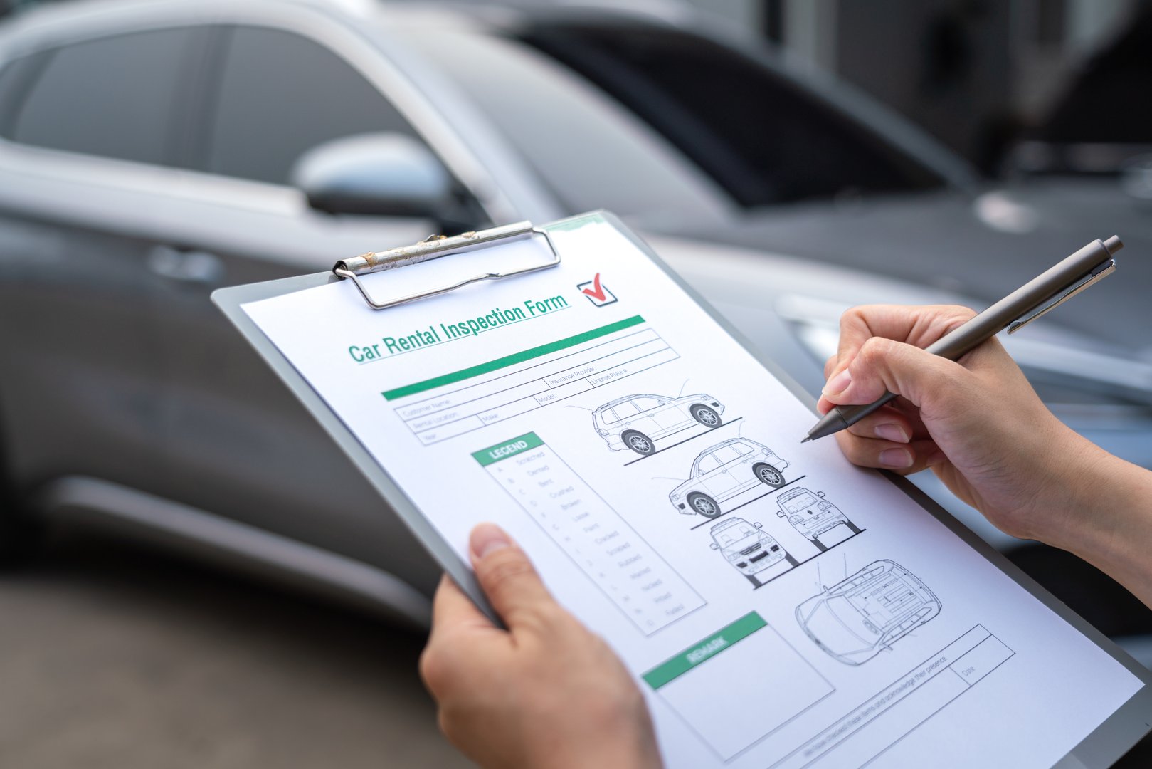 Action of a customer is signing on the agreement term of car rental service. Close-up and selective focus a human's hand with blurred background of cars in row. Business and transportation concept.
