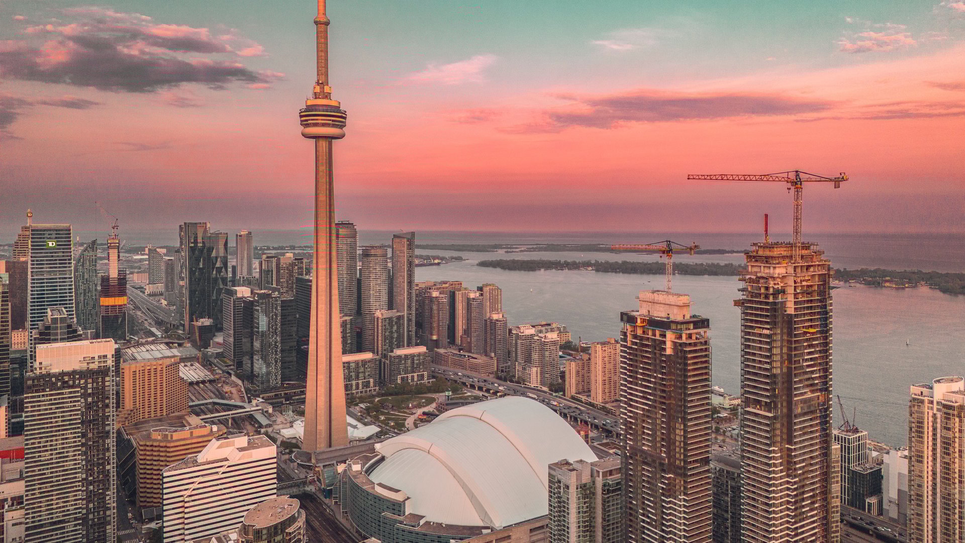 Aerial view of Toronto skyline with CN Tower and Lake Ontario at sunset, showcasing urban architecture and vibrant skies.