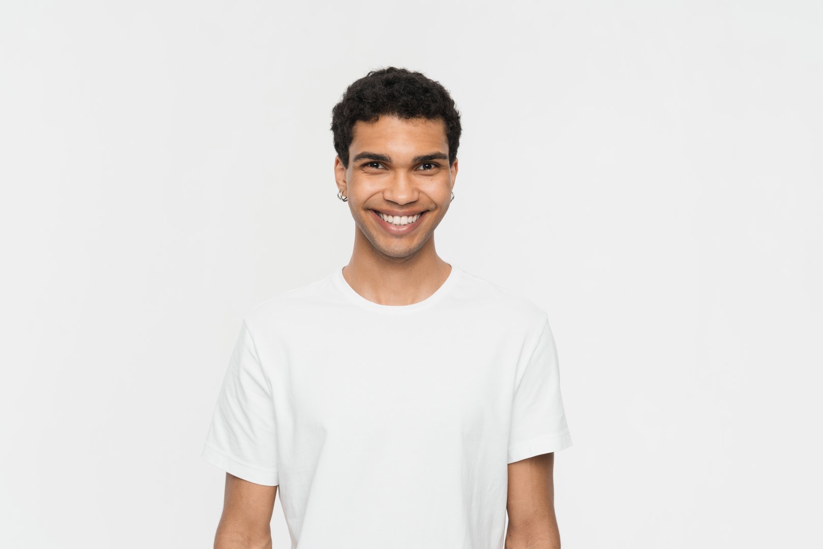 Portrait of a youthful man smiling warmly, wearing a white t-shirt, set against a pristine white backdrop, enhancing his cheerful demeanor and positive energy.