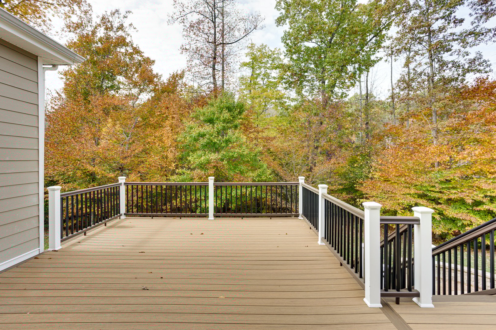 A spacious wooden deck attached to a house, bordered by a simple railing and overlooking a vibrant autumn forest, capturing the essence of tranquility and nature's beauty.