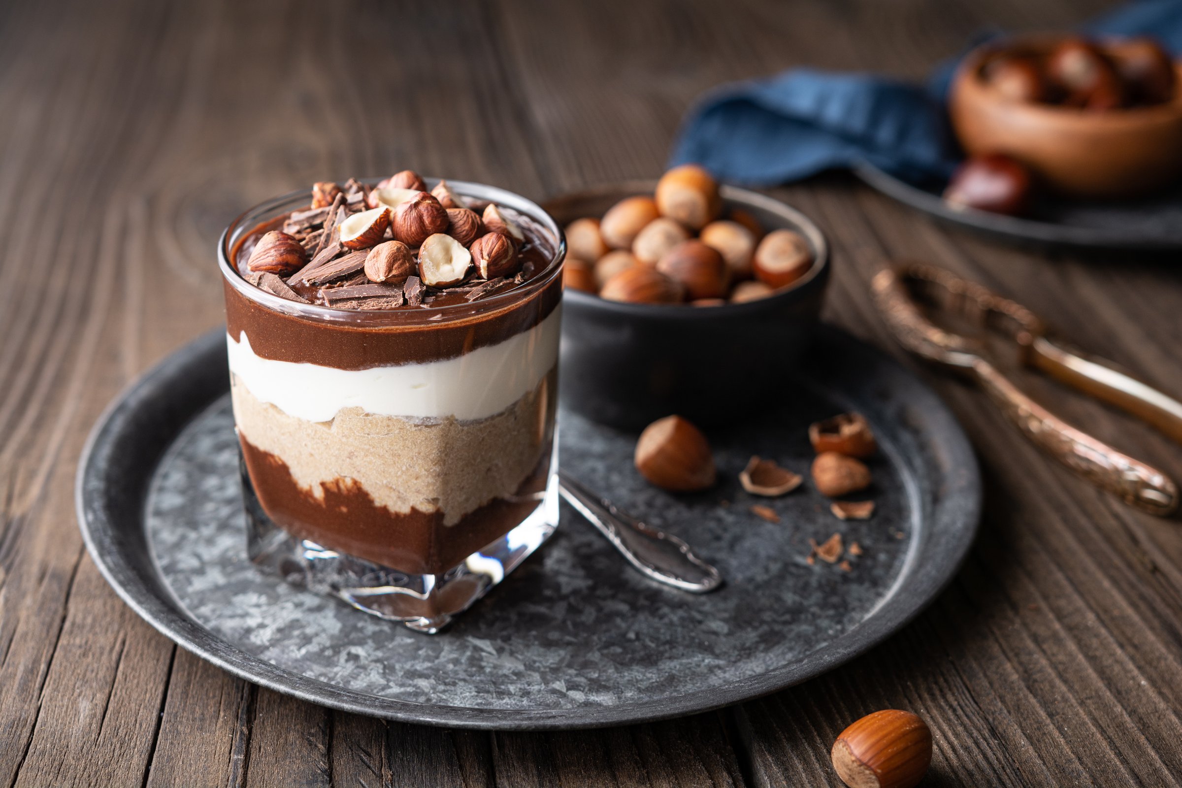 Layered dessert with chocolate mousse, cream cheese and whipped cream mixed with chestnut puree, topped with hazelnuts in a glass jar on rustic wooden background