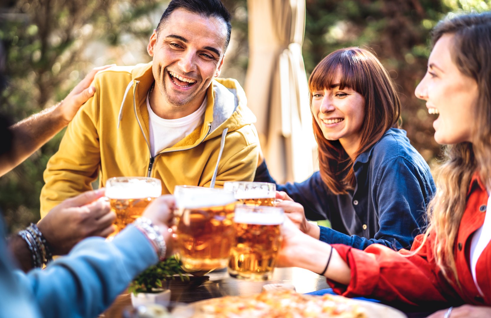Young friends drinking and toasting beer pints at brewery bar garden out side - Beverage life style concept with guy and girls having fun together at happy hour - Bright filter with focus on left man