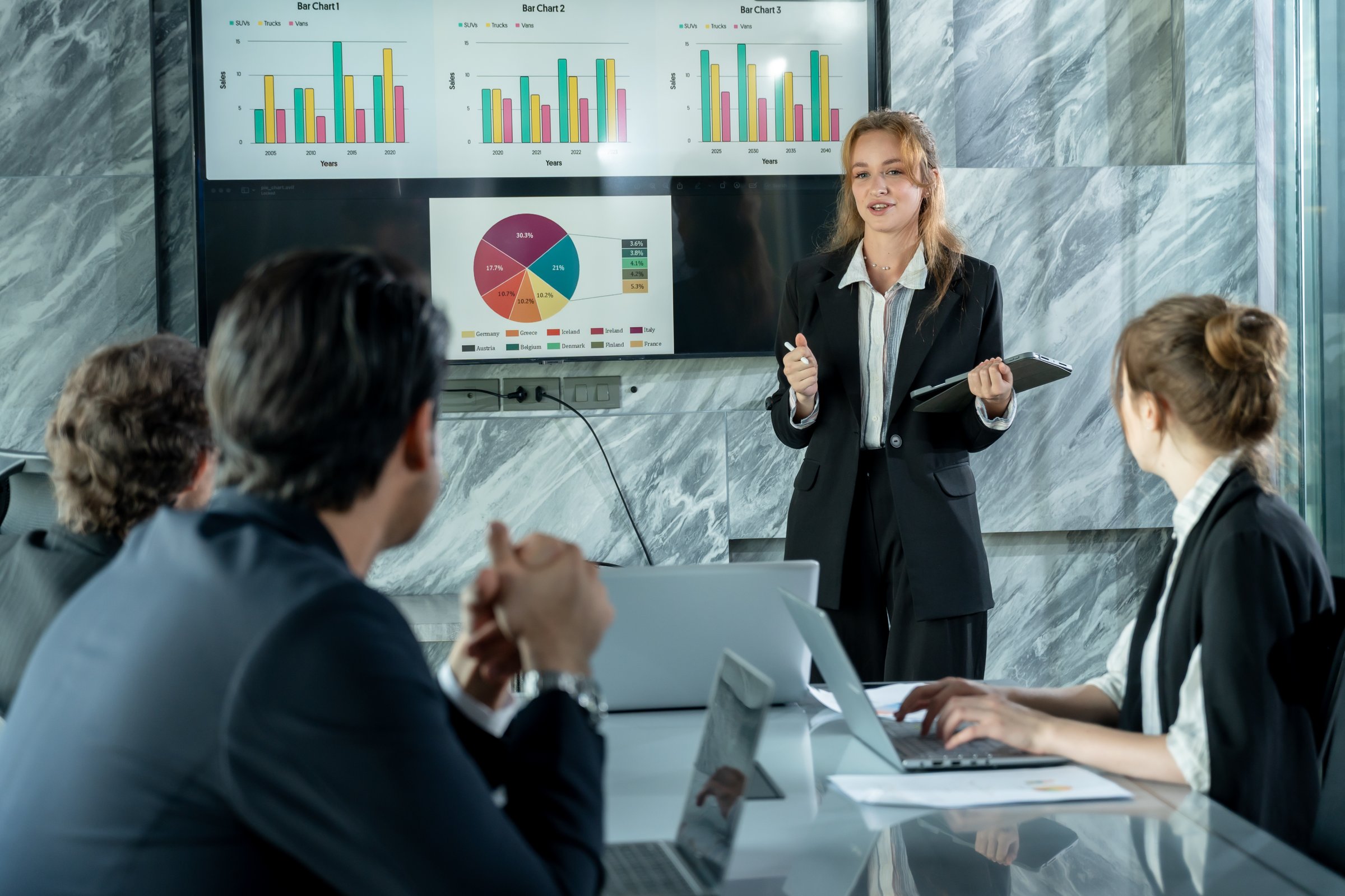 Female business presenter standing front digital board leading strategy meeting with multiracial colleagues listening analyzing financial data during team collaboration corporate session