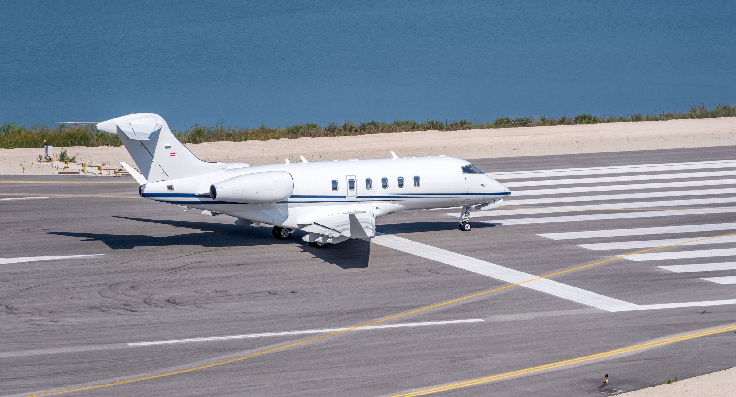 A sleek white private jet taxis on the coastal runway. Sunny day, calm blue water. Corfu airport Greece , Chalkiopoulos Lagoon