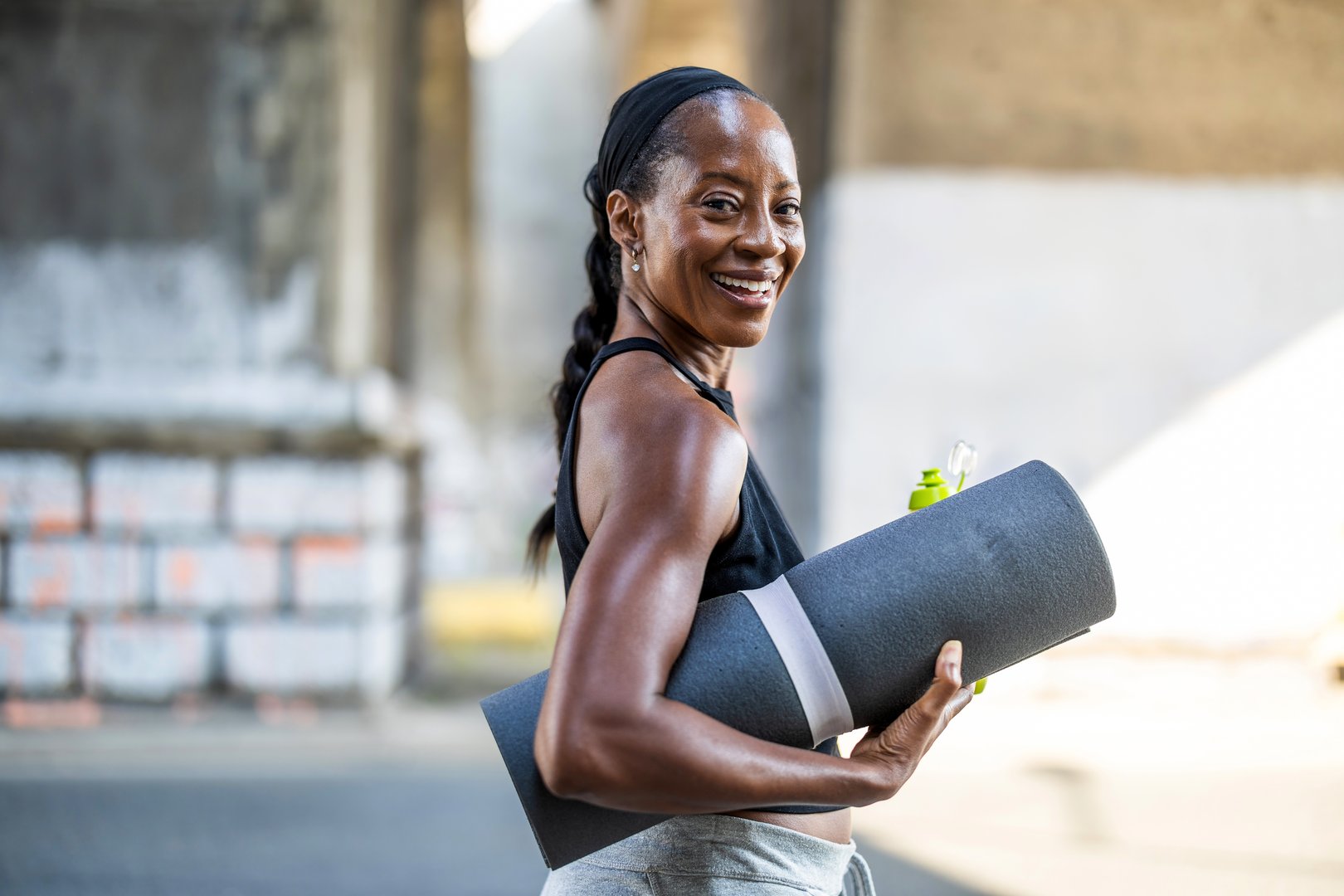 Smiling woman holding an exercise mat in the city street