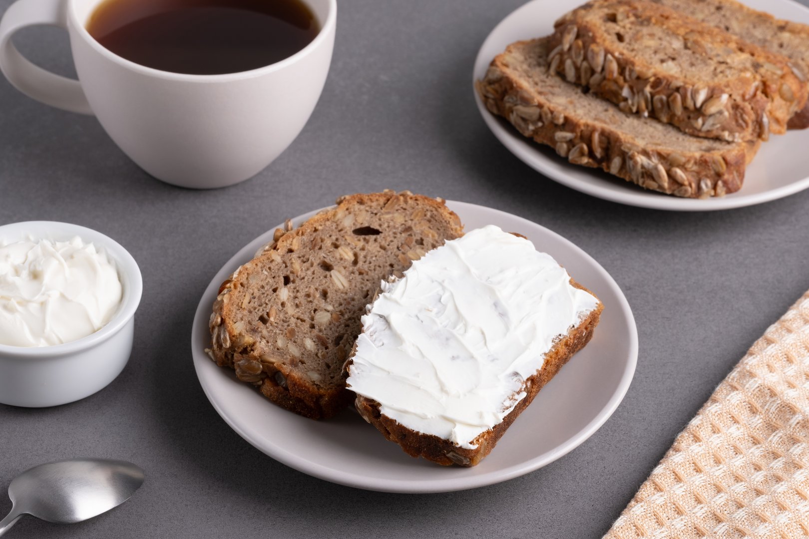 Slices of whole grain bread topped with cream cheese on a plate in a cozy kitchen setting.