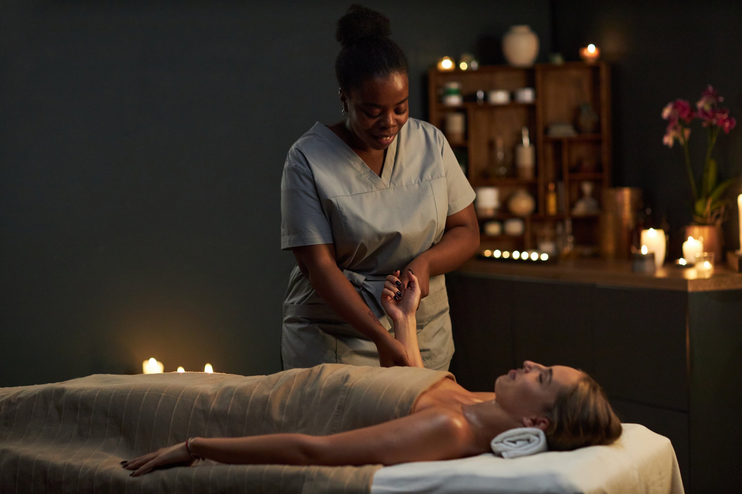 Masseuse providing relaxing massage in tranquil, dimly lit spa setting enhanced by candlelight and serene atmosphere creating peaceful environment