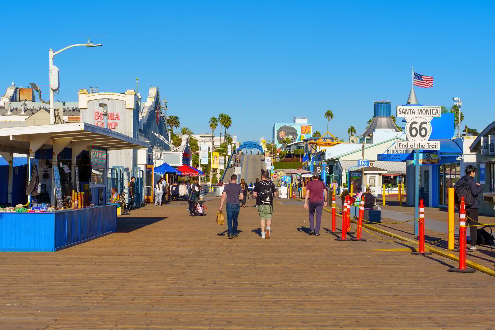 Santa Monica, California - January 16, 2025: Lively Santa Monica pier boardwalk scene featuring tourists strolling past colorful shops and food stands under clear blue skies, captured in bright daylight.