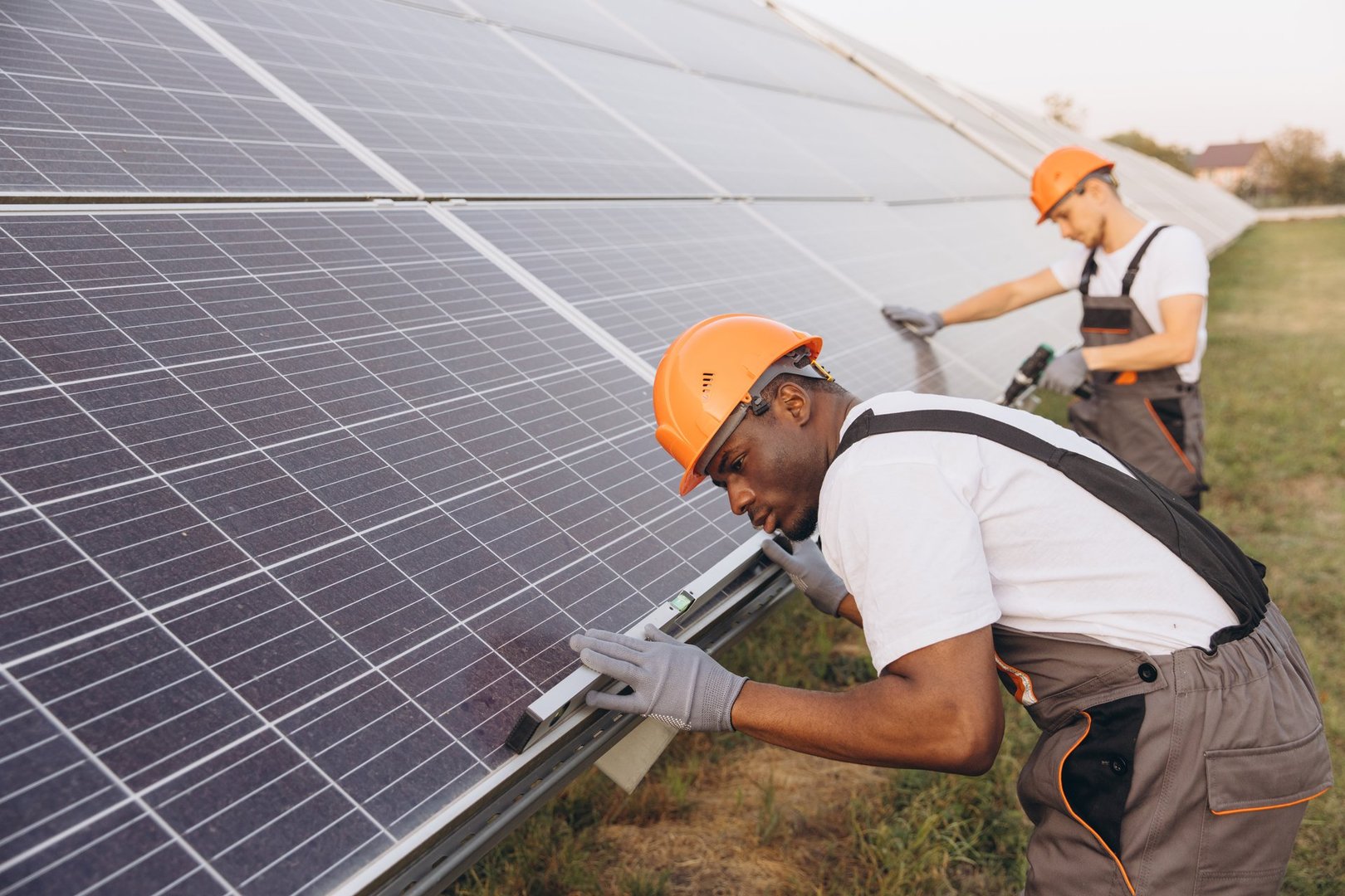 Two technicians in safety gear work on installing solar panels at a renewable energy facility. They are focused and methodical, showcasing teamwork and expertise in sustainable energy solutions.