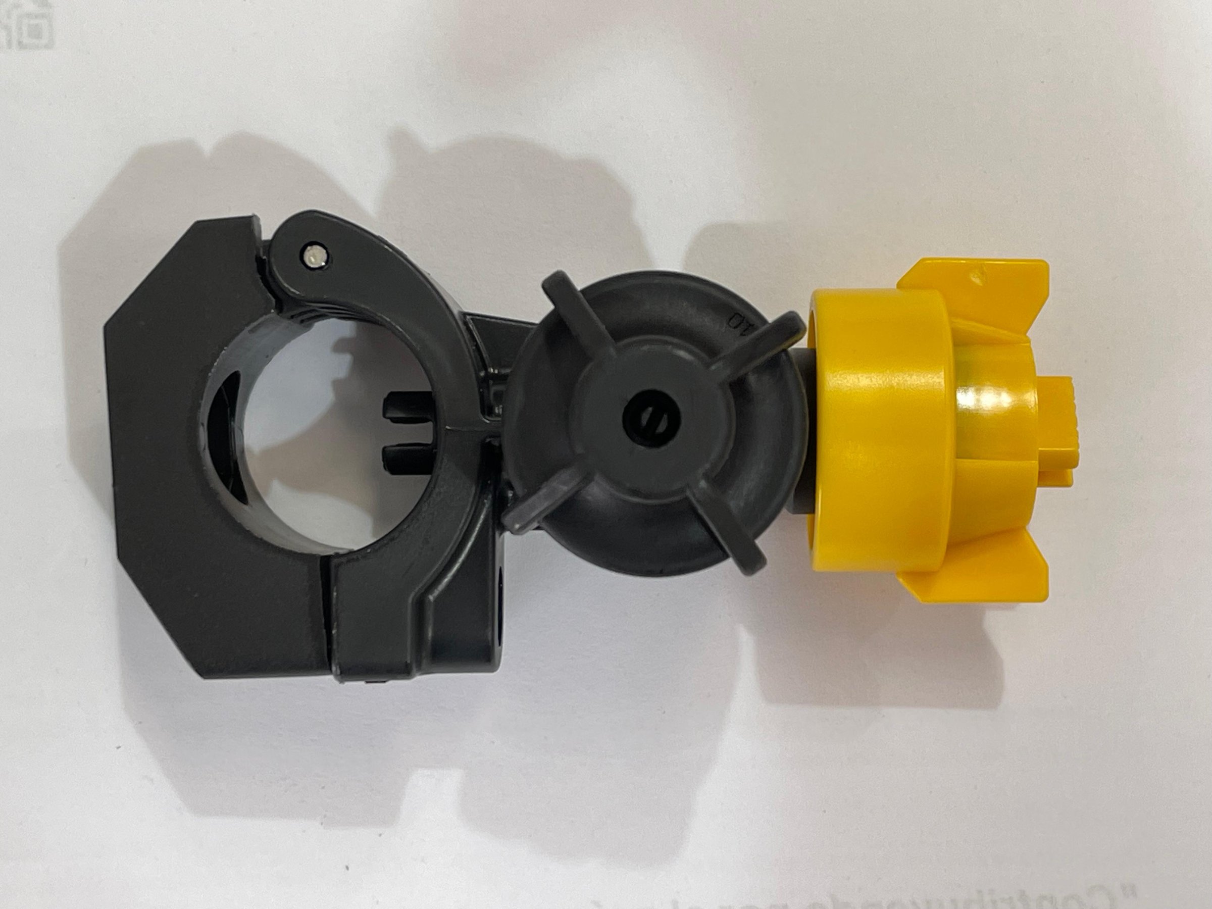 A plastic hose clamp with a yellow locking mechanism and black body lying on a white surface.