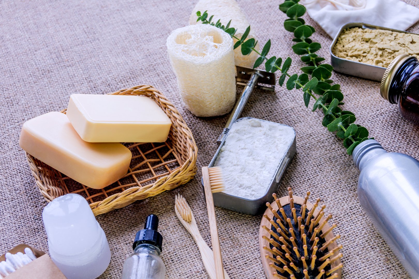 Bath accessories, personal care products in reusable packages. Loofah, bamboo teeth brushes, wooden ear sticks, deodorant crystal, powder on burlap background.