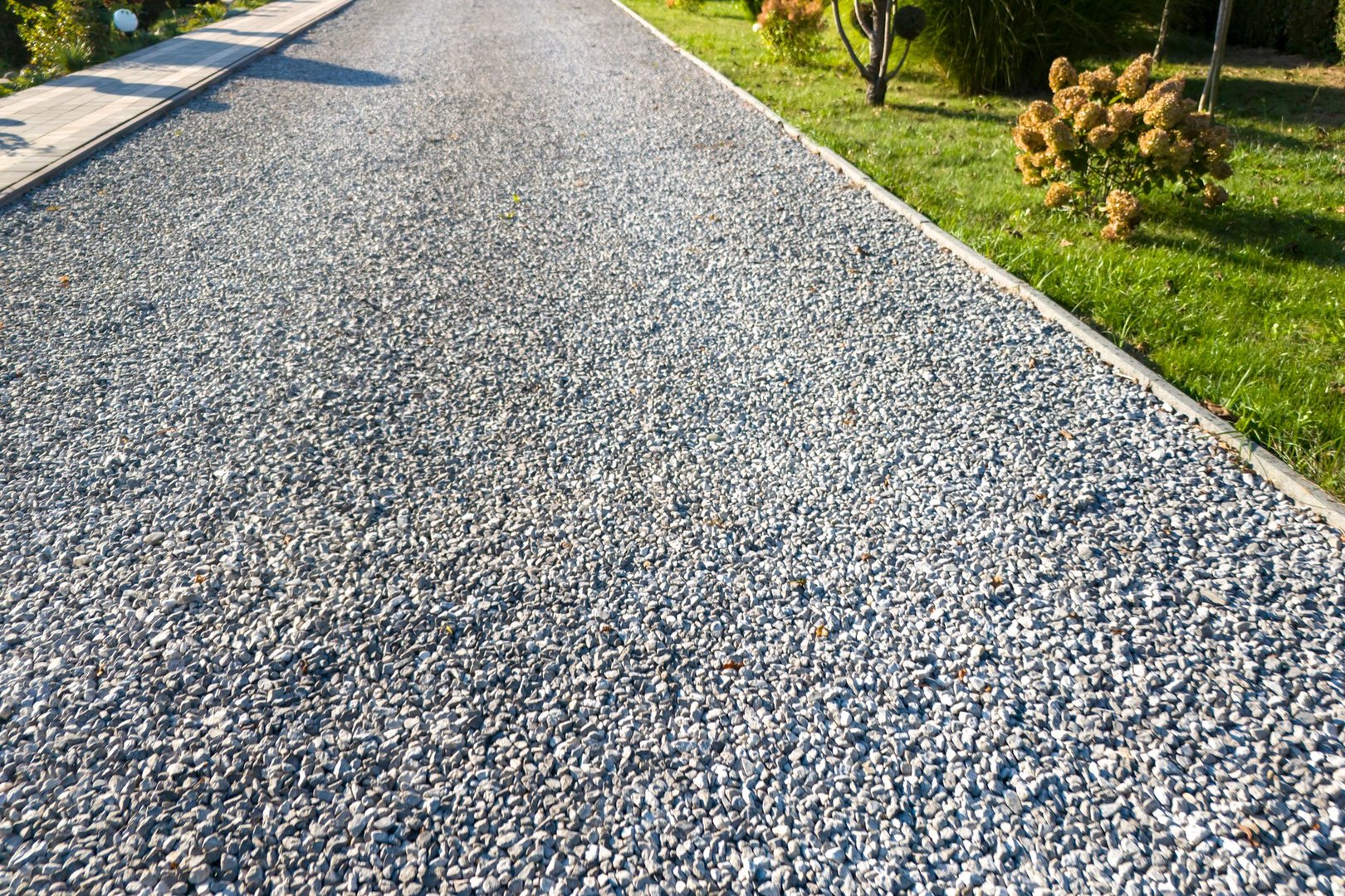 A view of a well-maintained gravel pathway surrounded by lush greenery and vibrant flowers, ideal for outdoor settings or landscaping projects.