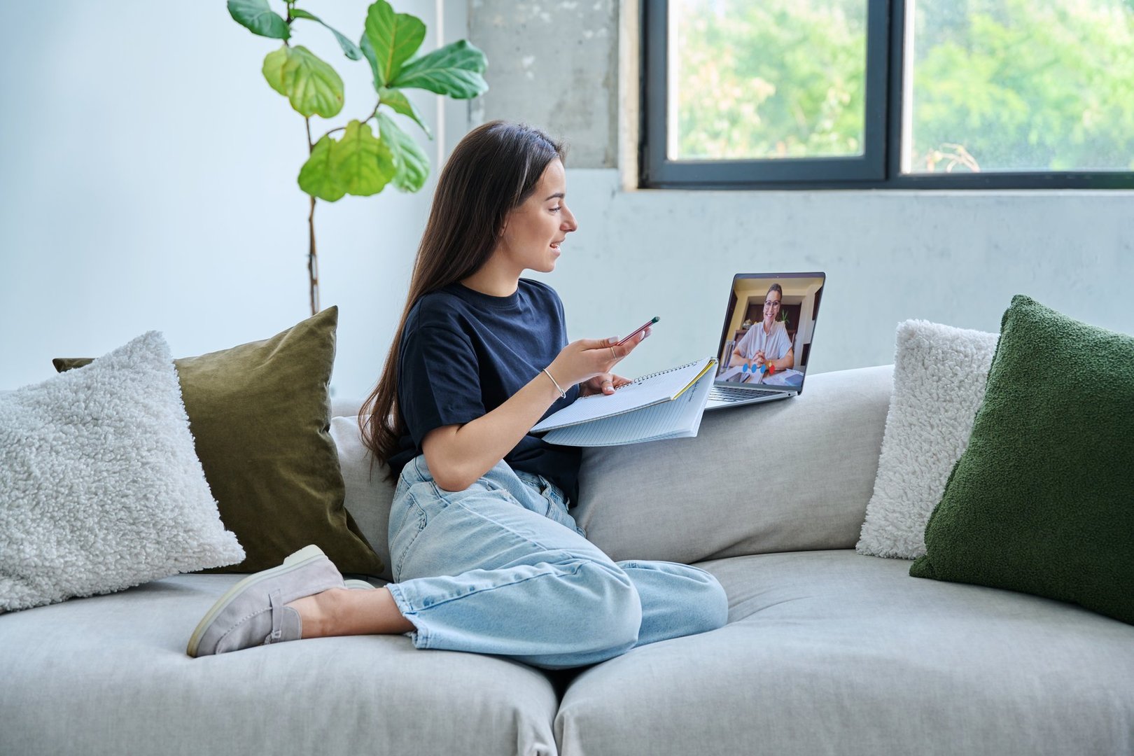 Teenage girl student having online therapy sitting at home on couch using laptop for video meeting with psychologist counselor