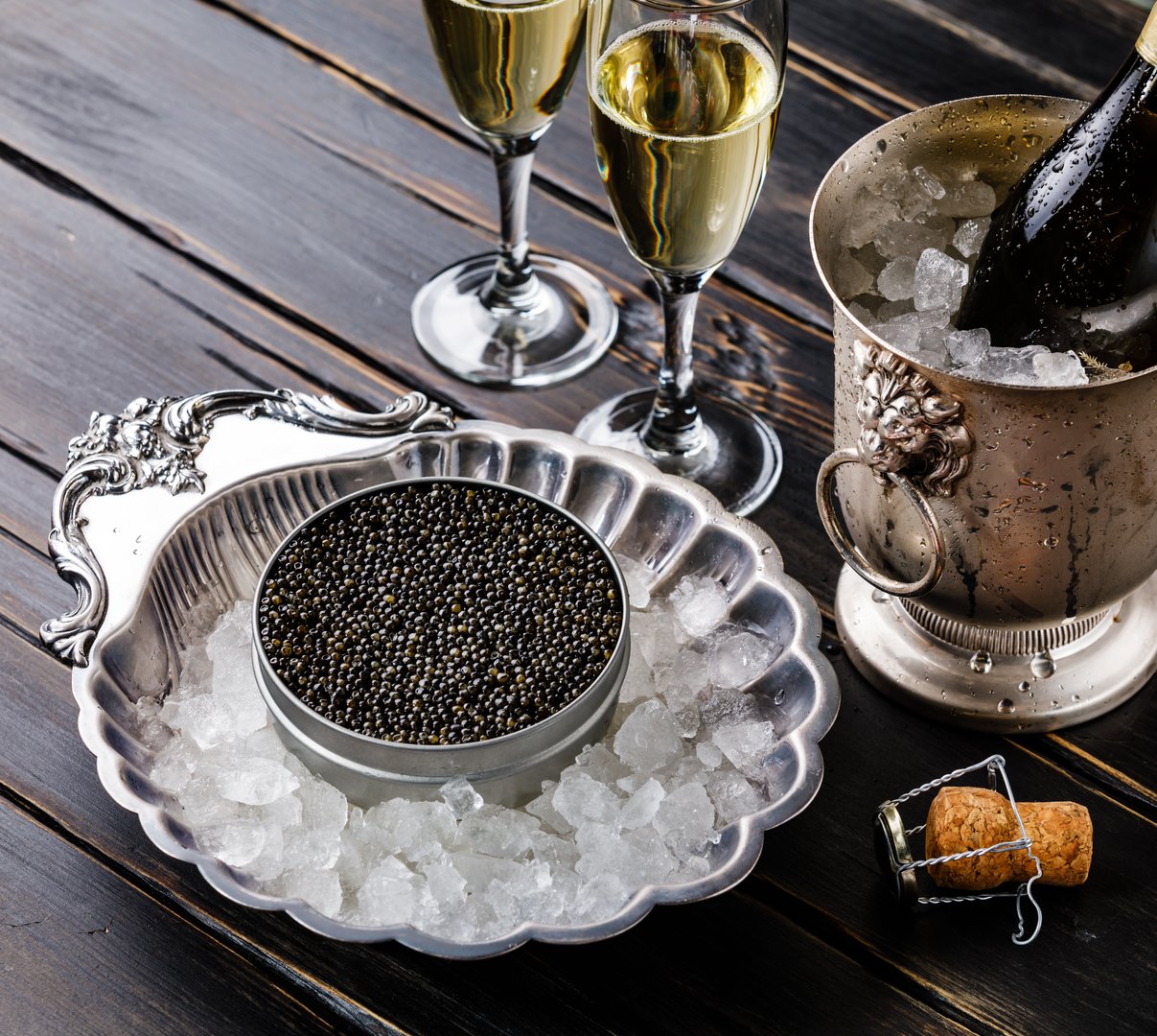 Black caviar in can on ice in silver bowl and champagne on black wooden background