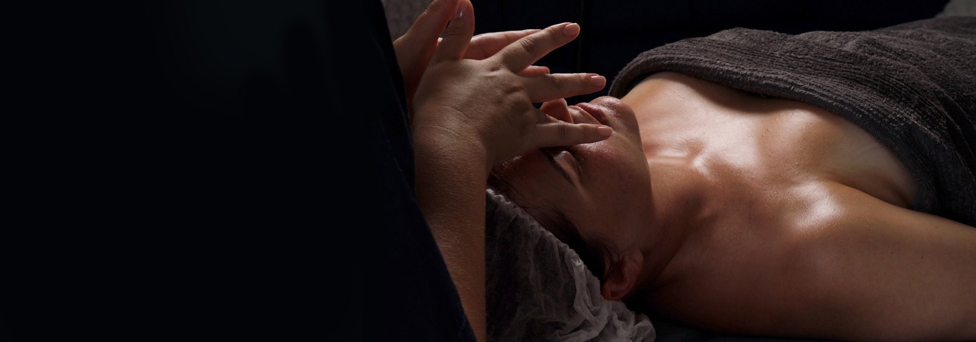 Woman receiving facial massage treatment in spa setting with towel and dim lighting.
