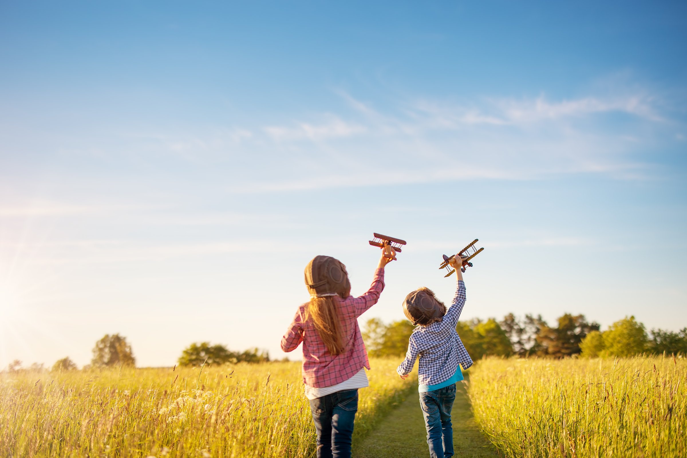 Boy and girl playing with wooden planes on the field in sunset. Concept of the family vacation, dreaming and friendship.