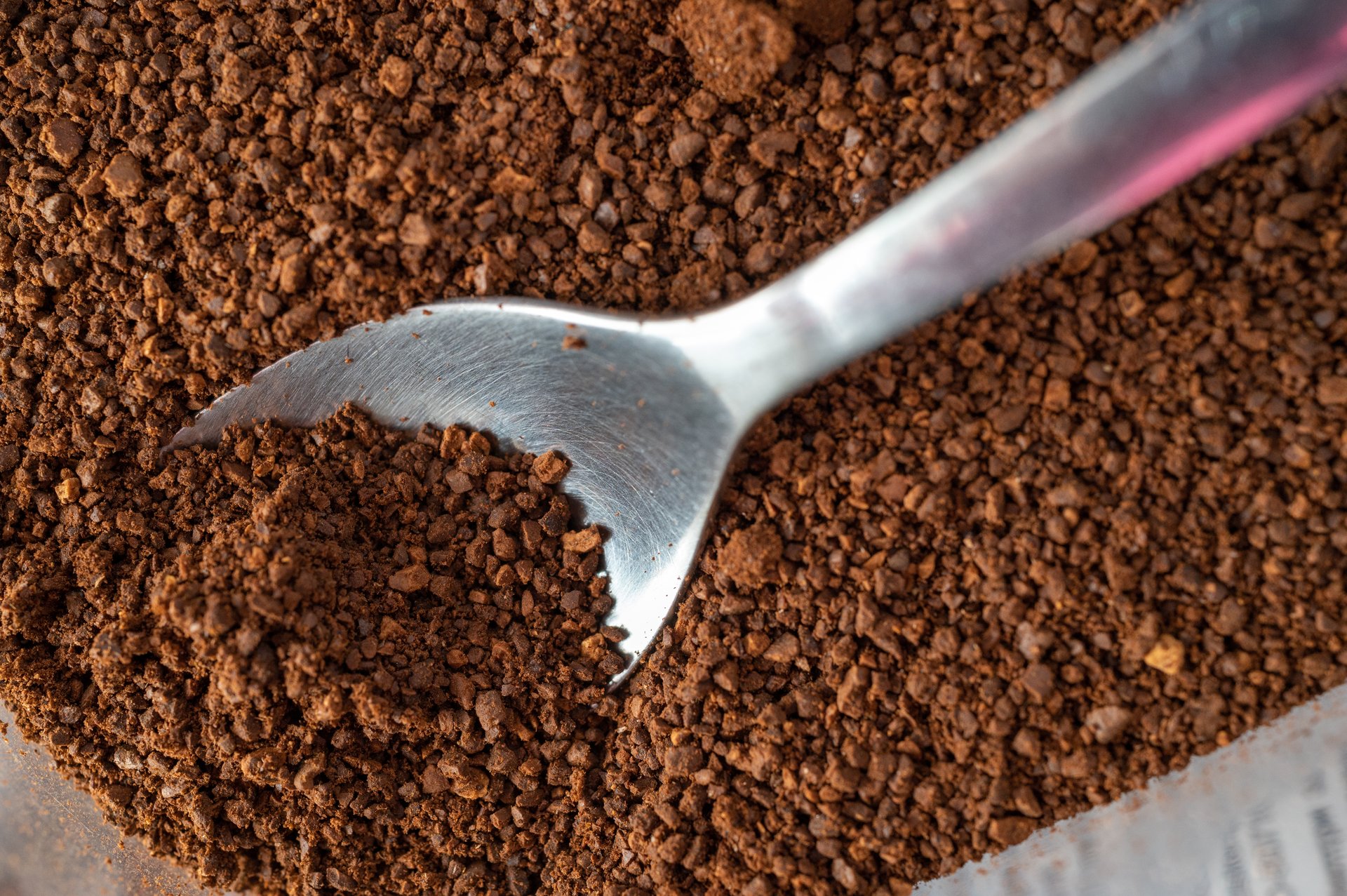 Close-up of ground coffee with a metal scoop, showing texture of coffee particles.