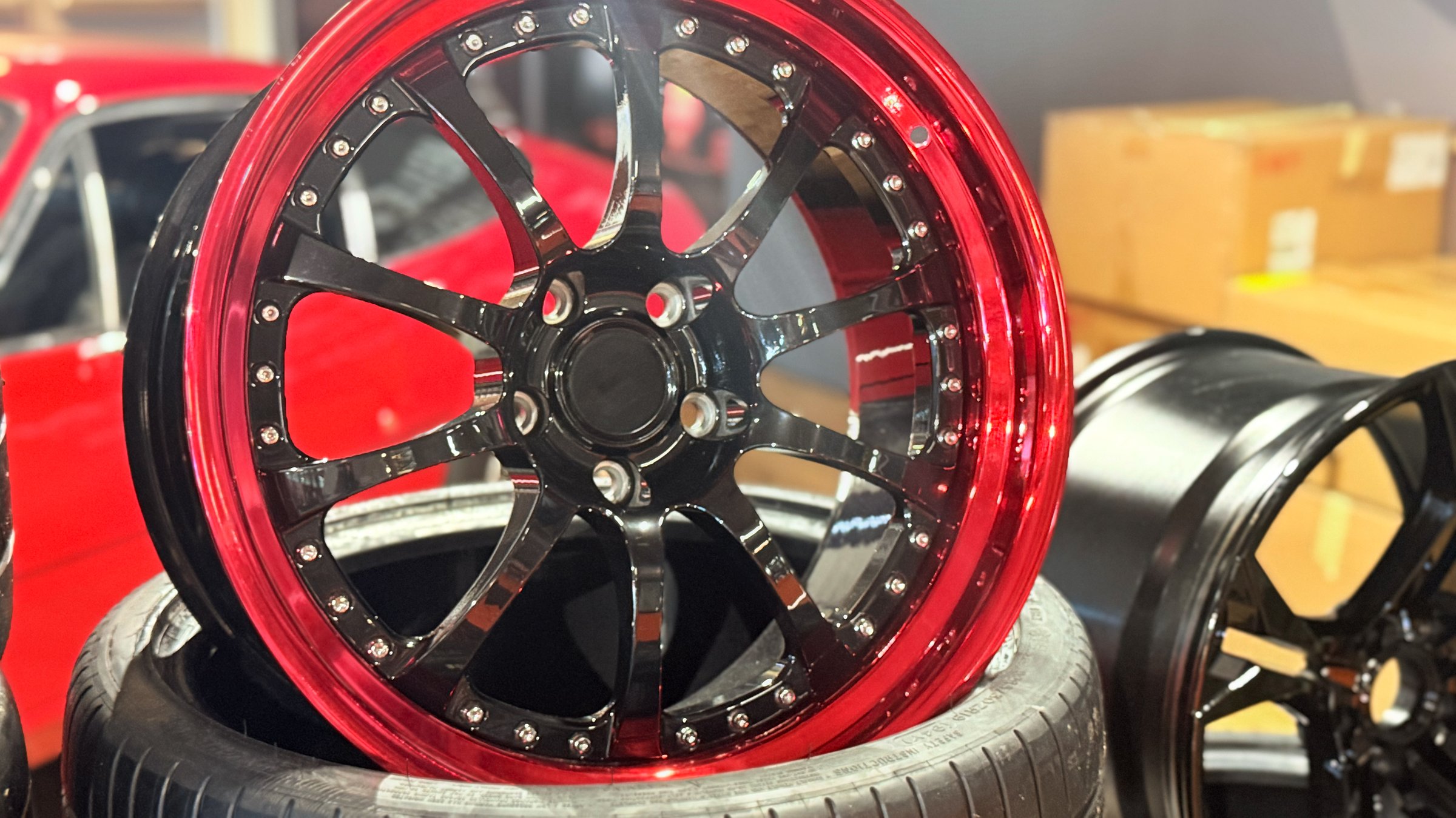 An automotive alloy wheel is displayed on a tire in a workshop. The rim is photographed front on, showing the central hub and thin spokes. Indoor lighting and shallow depth of field blur the background. The clean composition emphasizes product detail, suitable for car service, tuning, and parts catalogs. Listings.