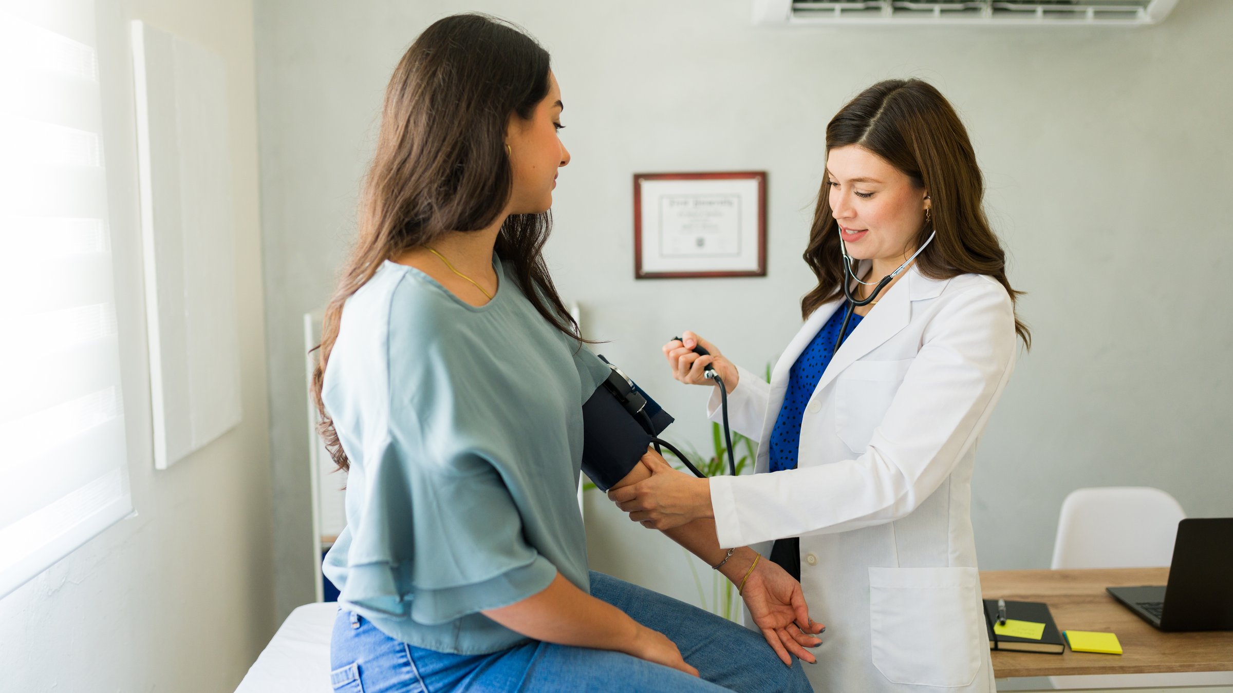 Young adult female doctor is taking the blood pressure of a female patient during a medical consultation