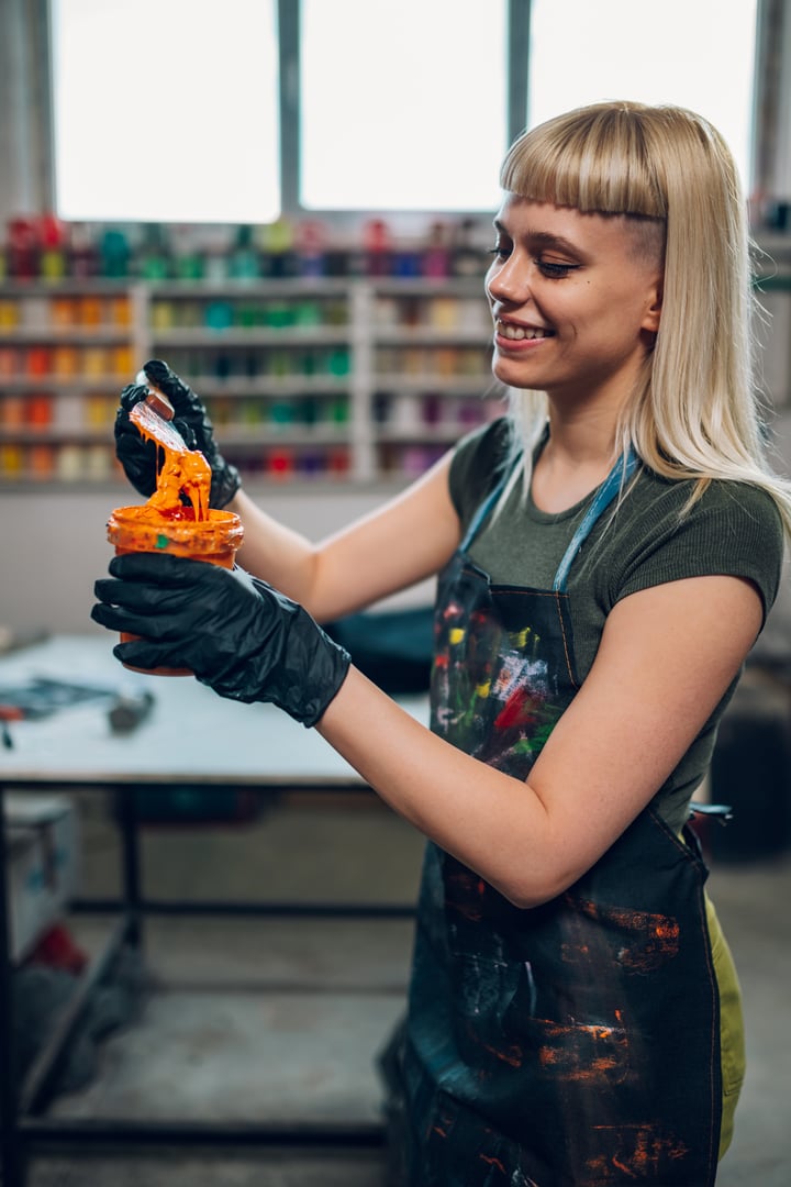 Artista plástica con pinceles y pinturas utilizando guantes de nitrilo negros.