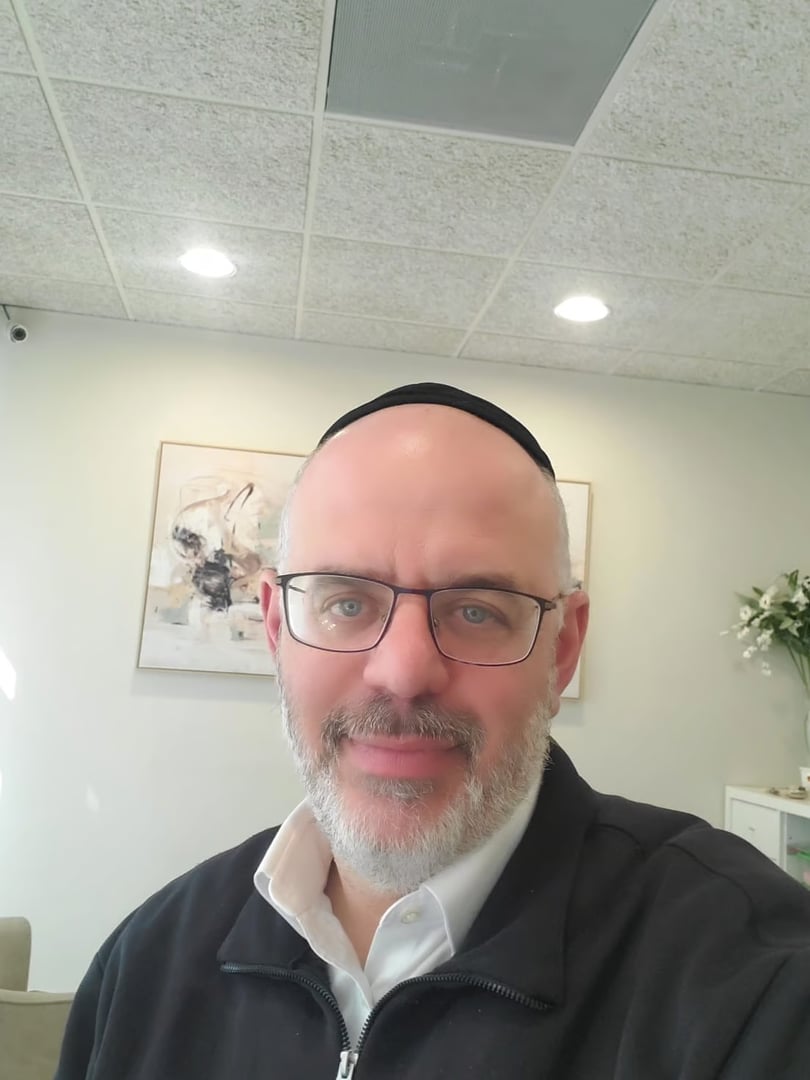 Man with glasses wearing a black skullcap and sweater in an indoor setting with soft lighting and wall art.