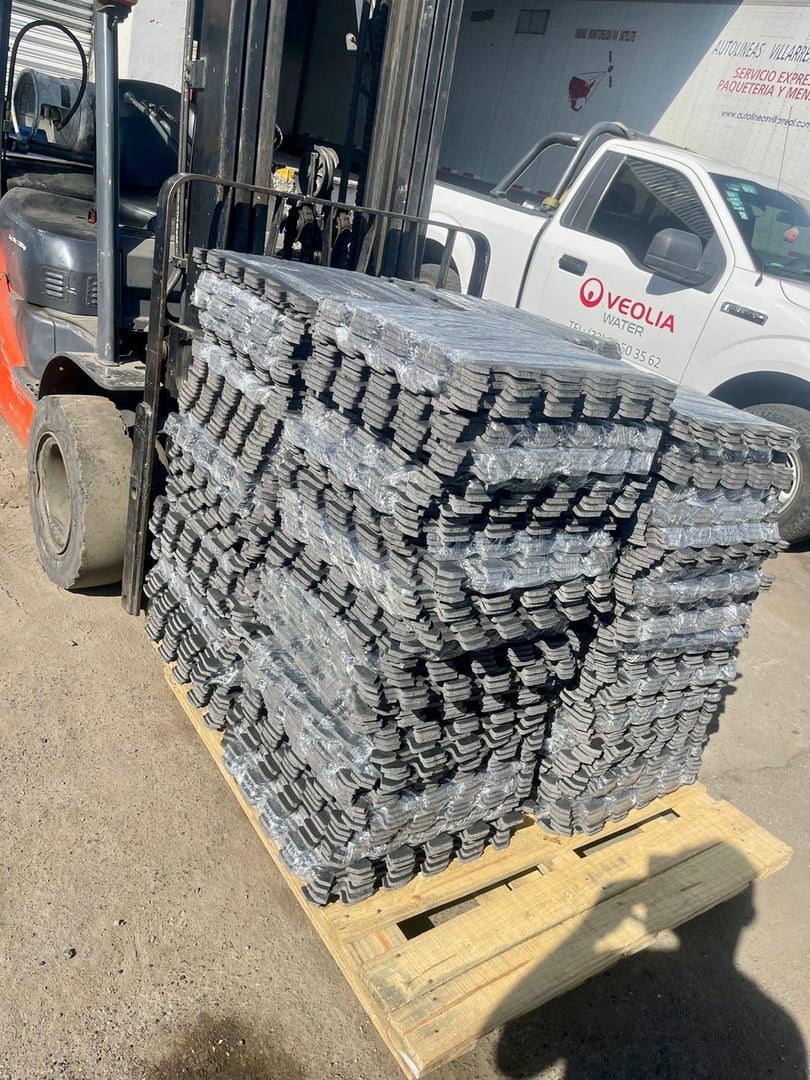 Forklift carrying a pallet stacked with bundles of metal sheets in an outdoor industrial area.