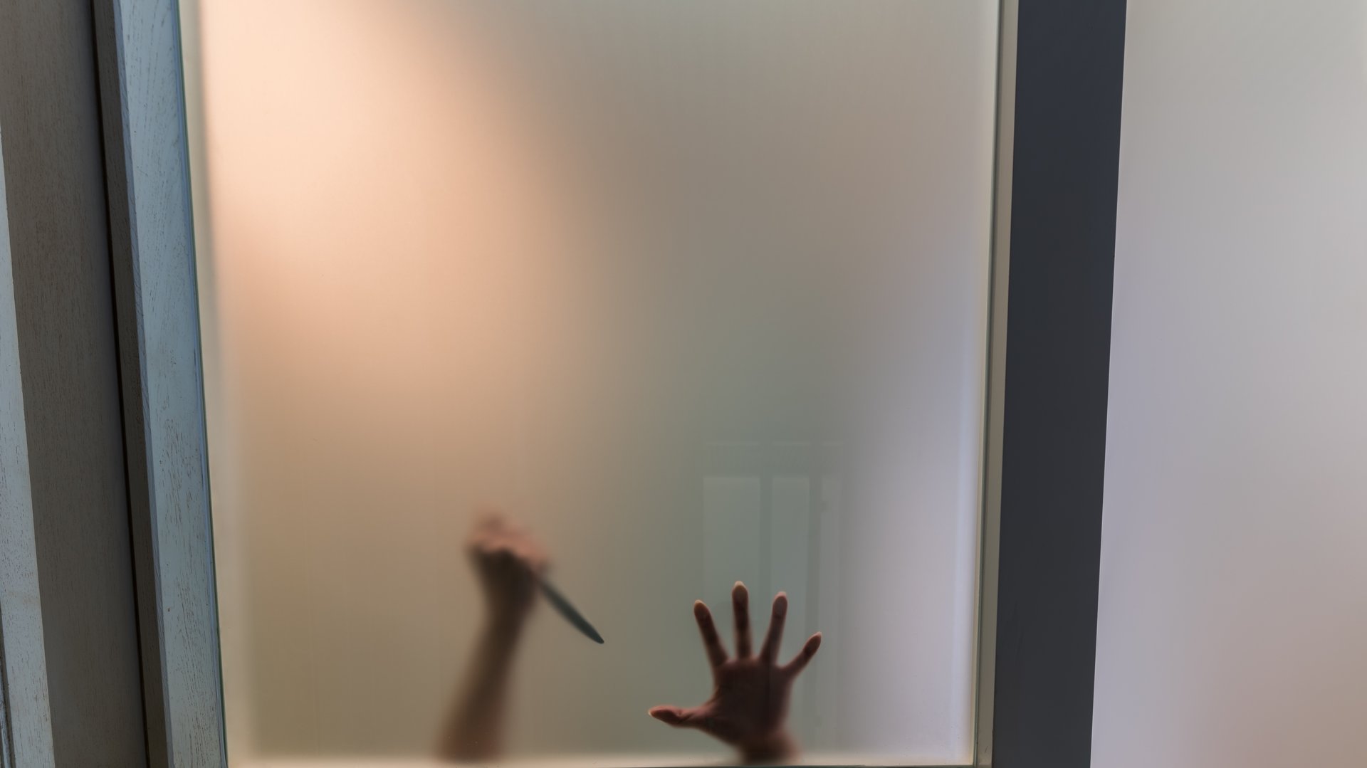 Blurry crime scene of shadow hand holding a knife behind the matte glass