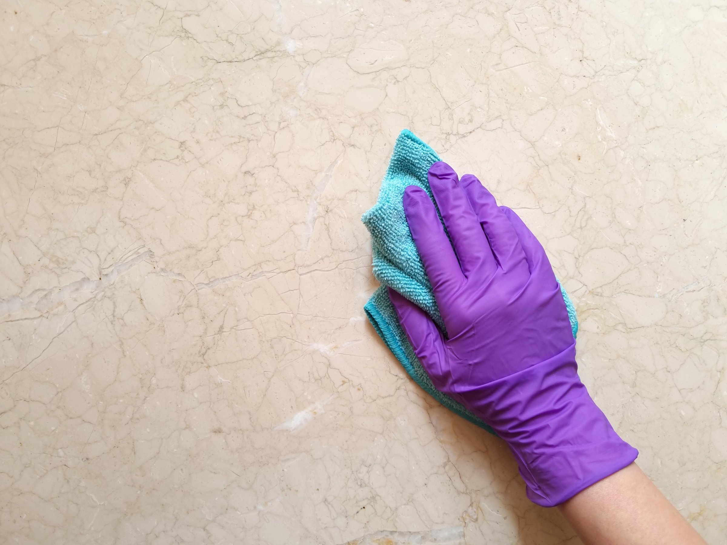 A girl's hand in a purple rubber protective glove wipes a marble surface with a colored cloth