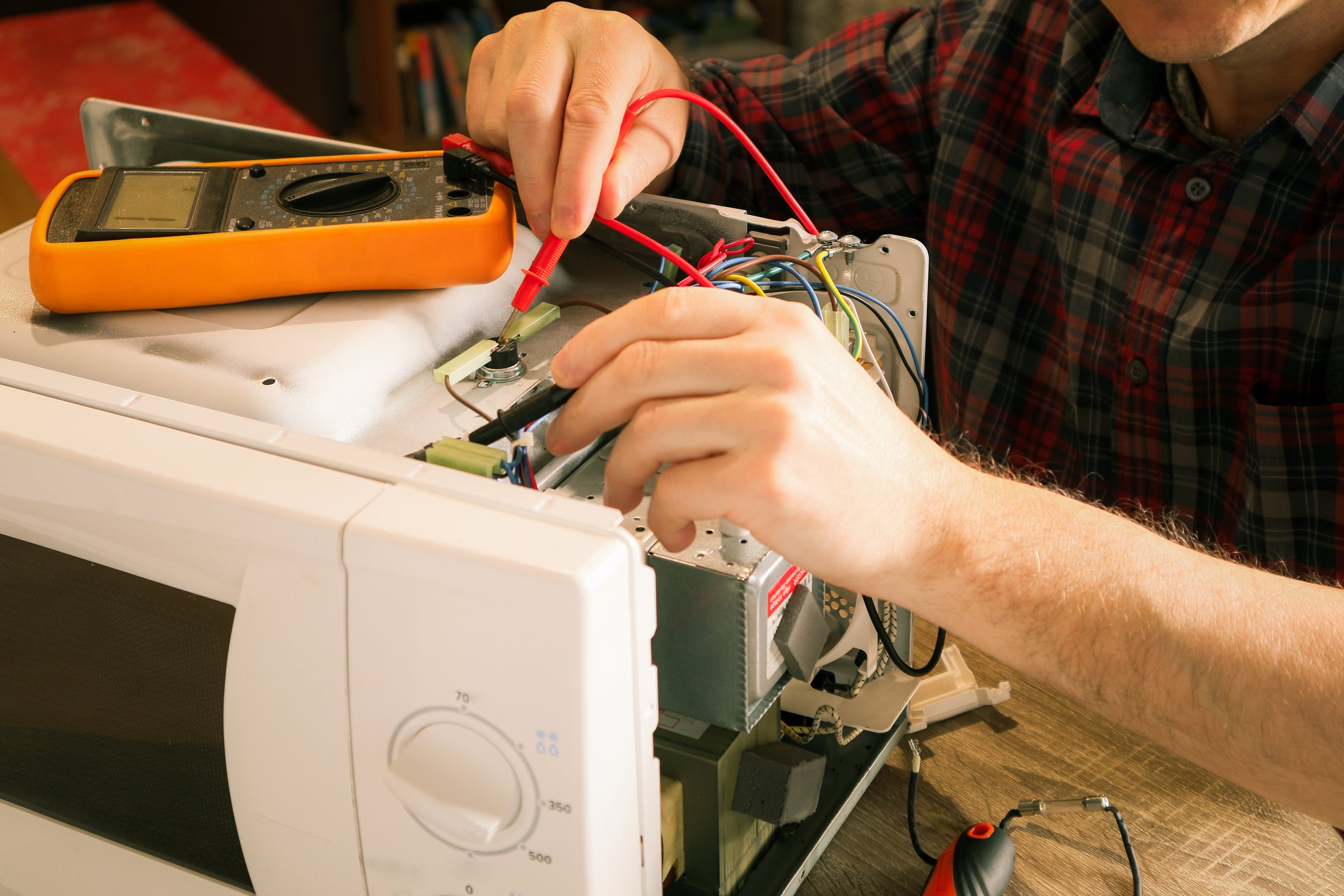 A repair engineer uses a multimeter to check the circuits of a microwave oven, looking for a fault. Diagnostics repair of microwave oven.