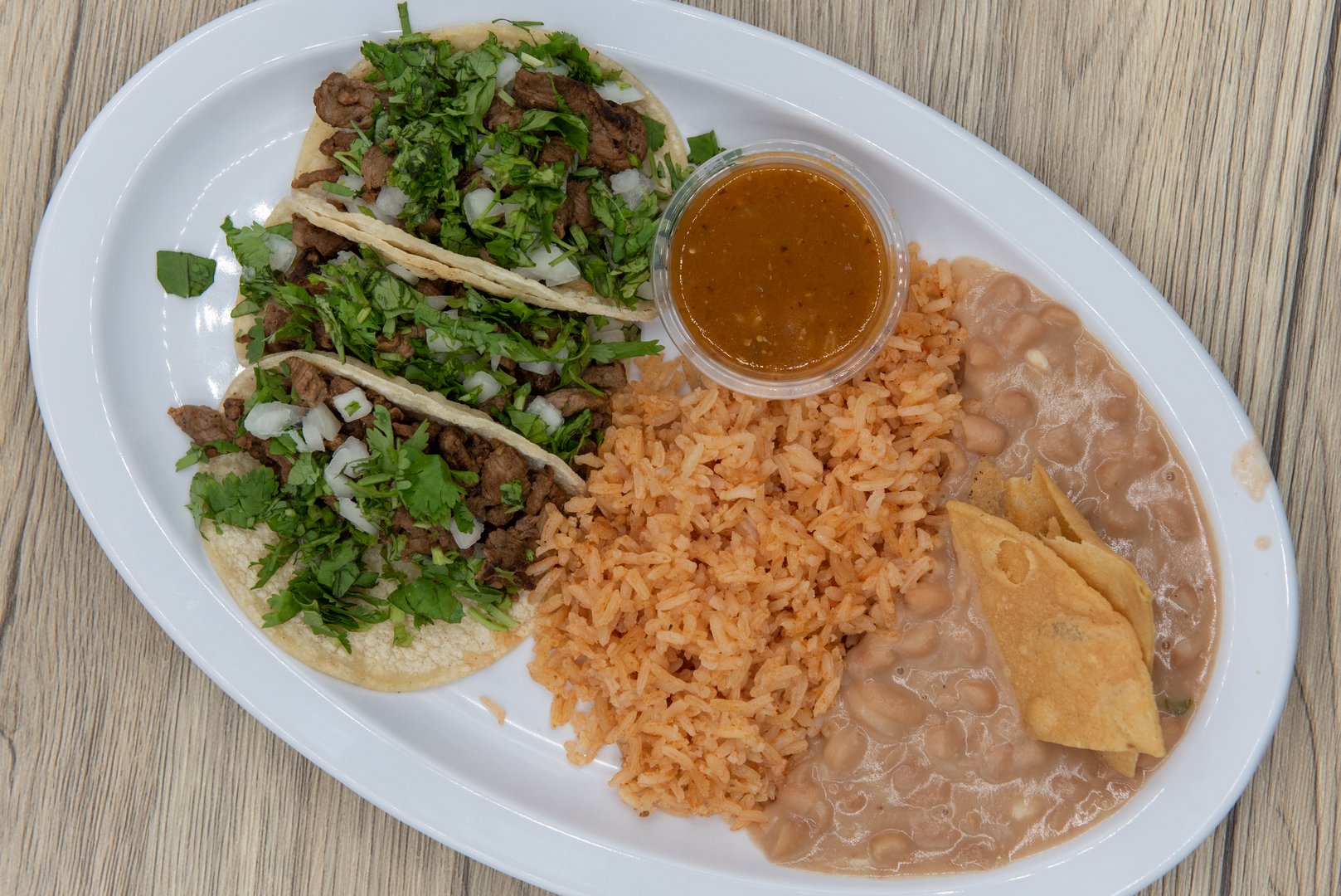 Overhead view of hearty plate of three loaded carne asada tacos with cilantro, served with rice and refried beans.
