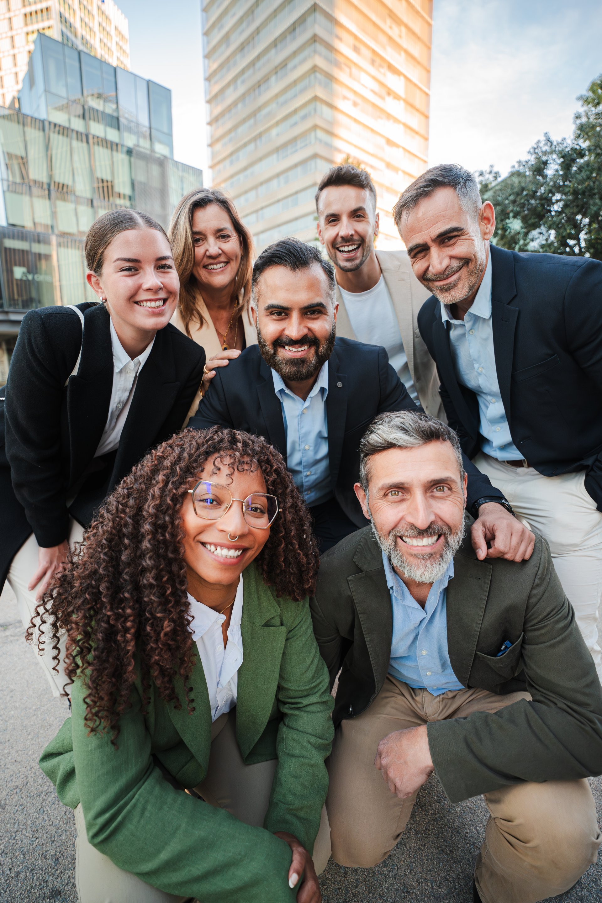 Vertical. Diverse group of business professionals smiling and looking at the camera during an outdoor meeting, showcasing teamwork. Successful businesspeople looking at camera together at the downtown. High quality photo