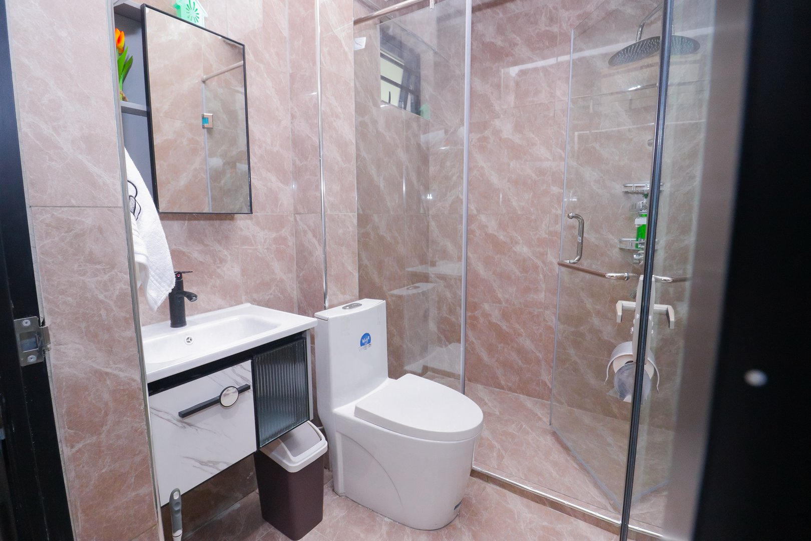 Modern bathroom with glass shower, tiled walls, wall-mounted sink, toilet, and a mirror above the sink.