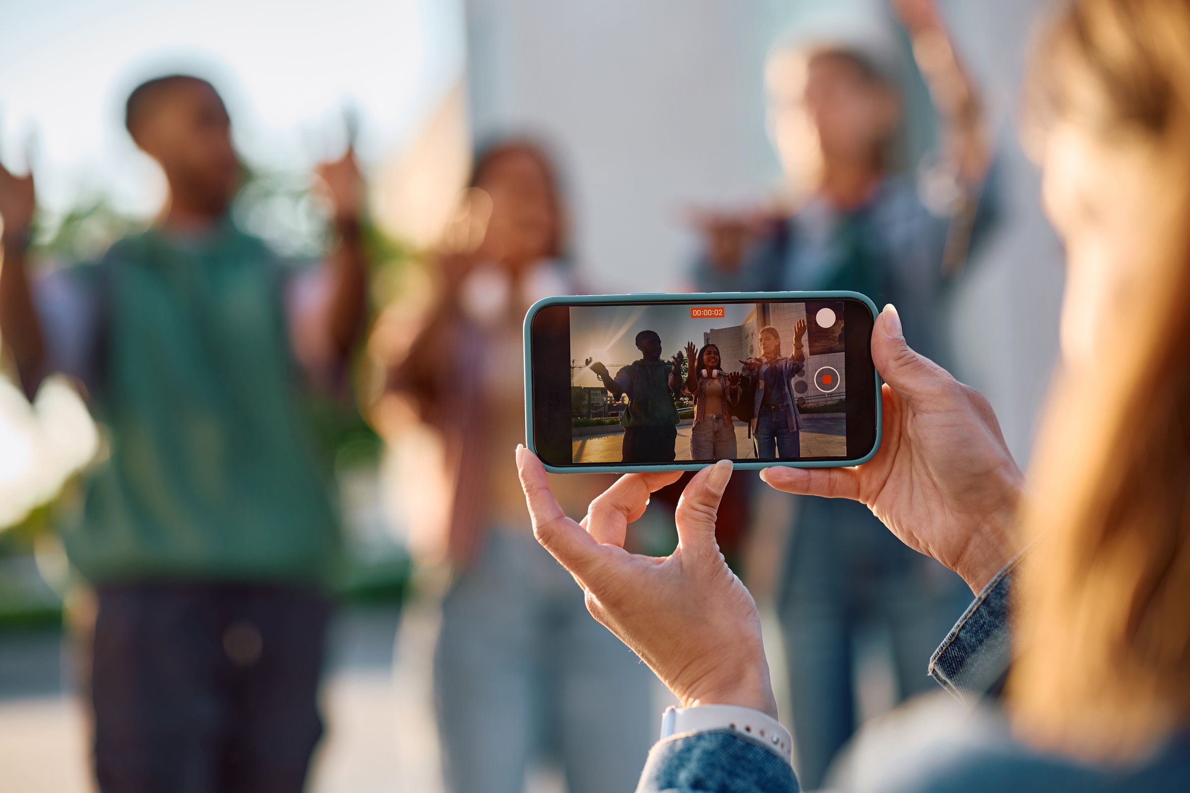 Close up of student filming her friends with smart phone at university campus.