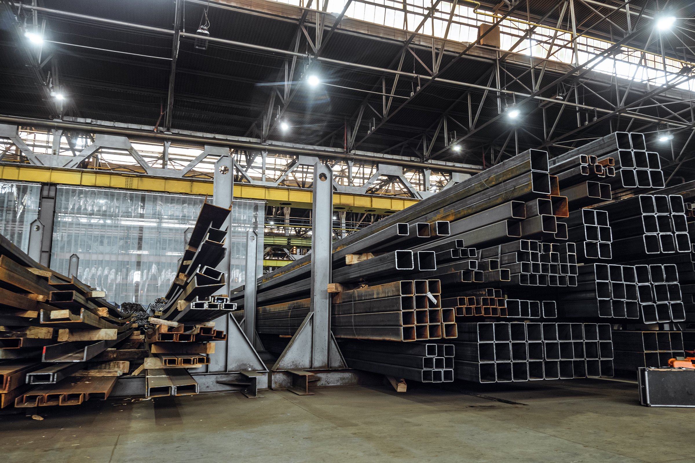 Warehousing workshop of rolled metal constructions in industrial metalwork production hall. Steel closed profiles metal structures in stack.