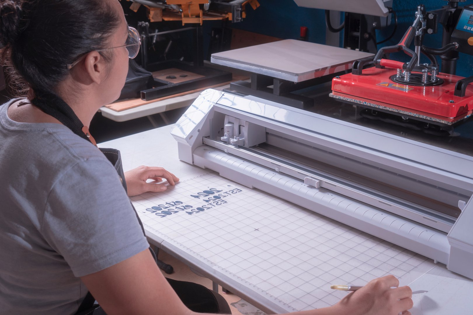 Young woman removes excess material with weeding tool, workplace with cutting plotter, tools, selective focus.