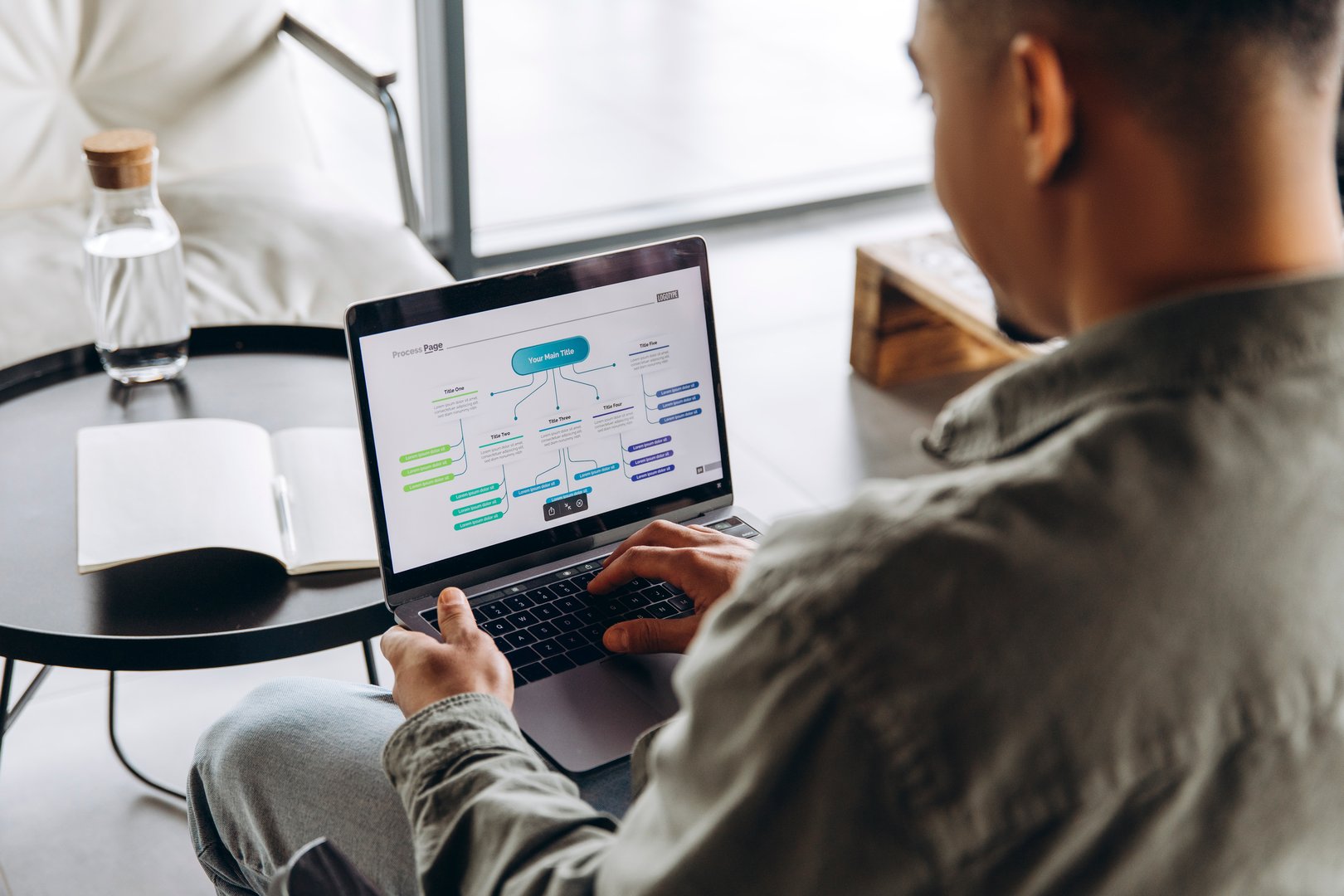 Businessman sitting comfortably in modern office, working on a flowchart presentation using a laptop, showcasing efficient project planning and workflow management. Online technology concept