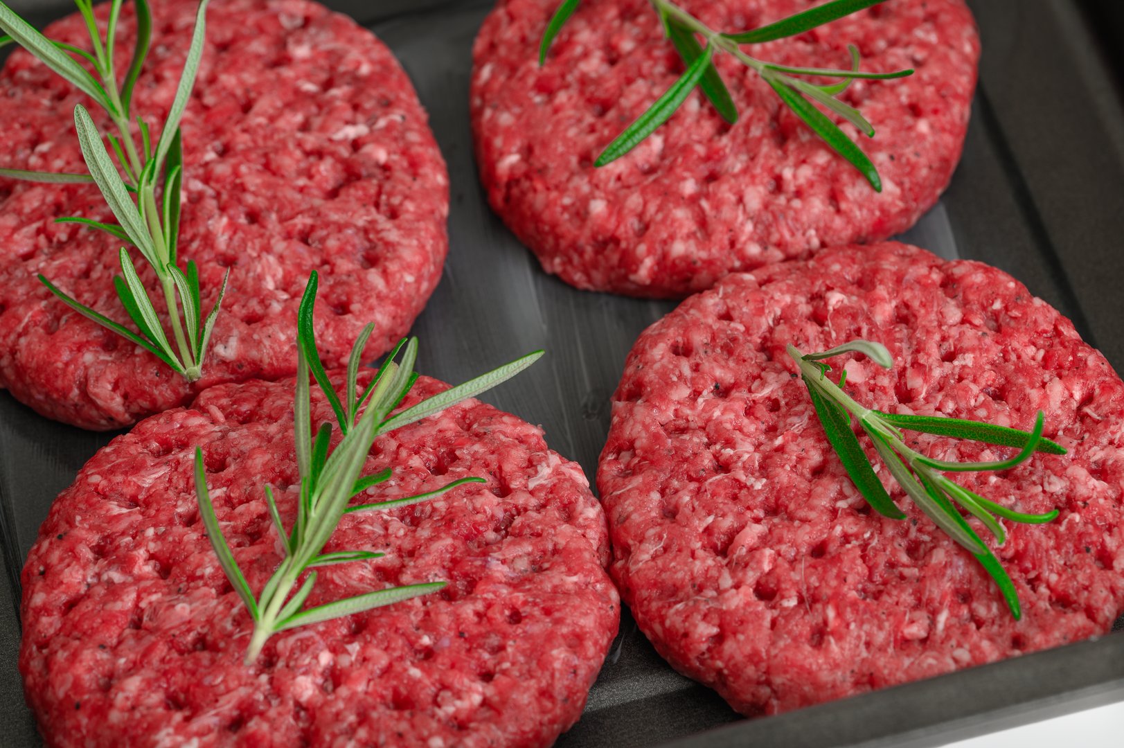 Four raw beef burgers close up