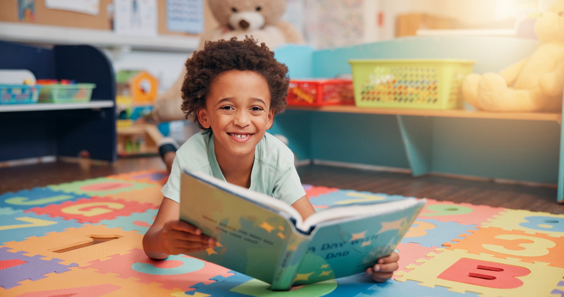 Boy, reading book and portrait on floor in classroom for development, story or knowledge at academy. Child, learning and study for scholarship, smile or info with course at elementary school