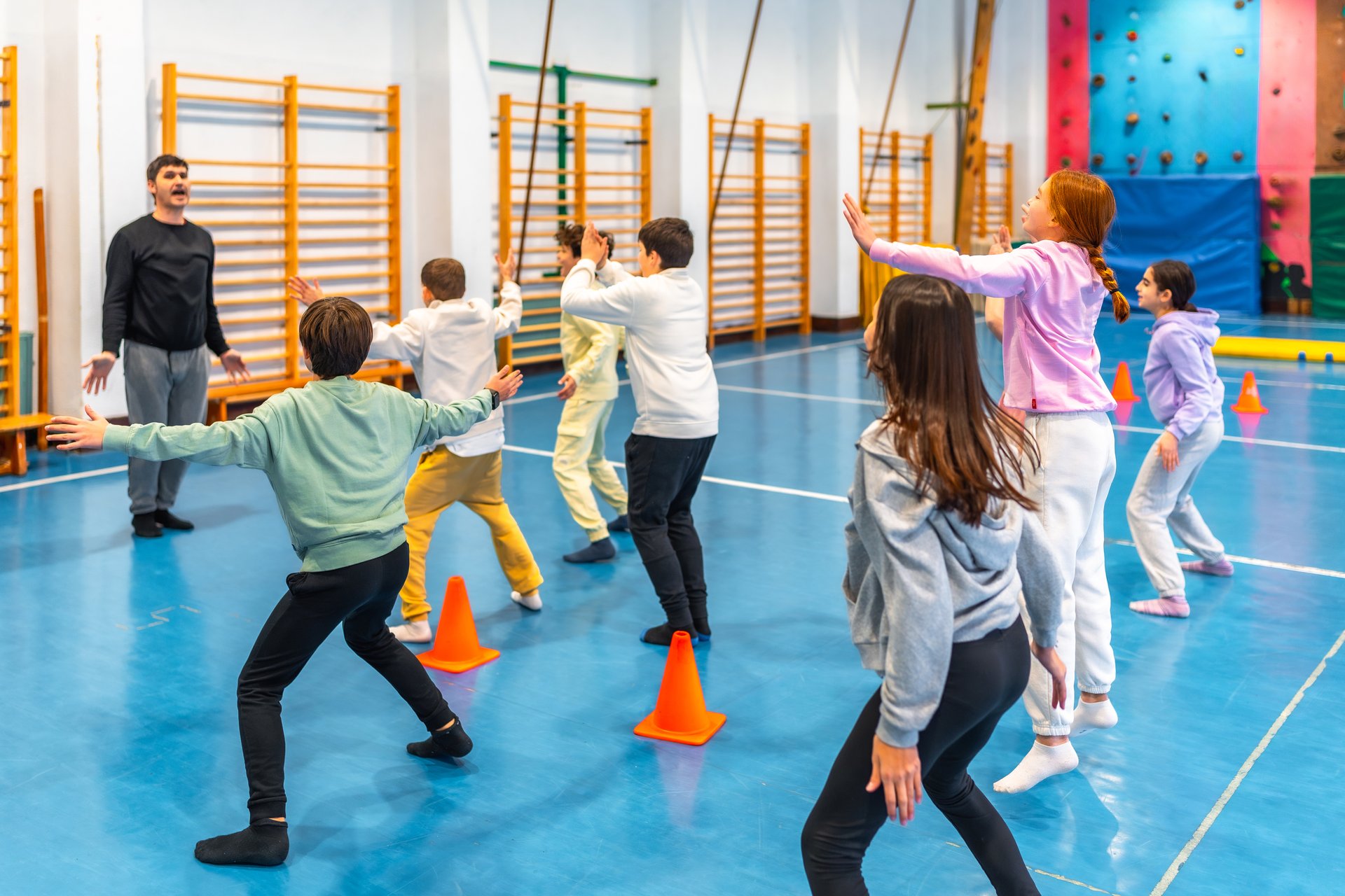 Elementary school students practicing gymnastics exercises with their teacher in the school gym