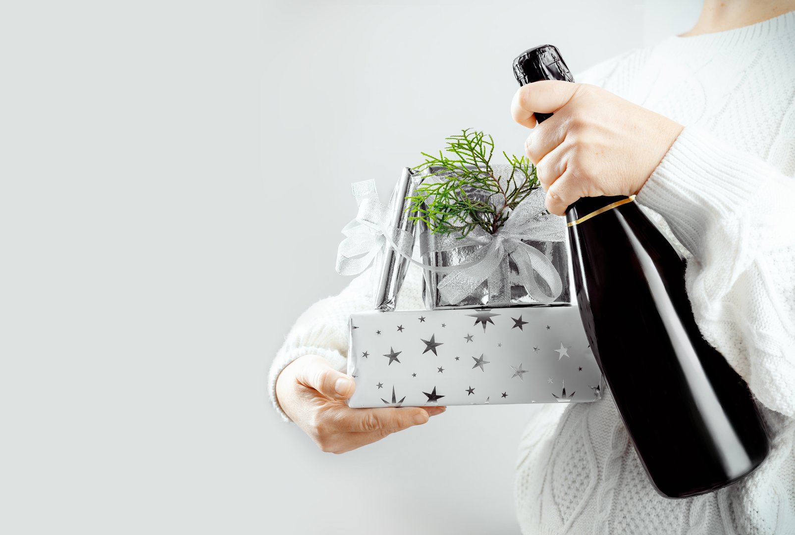 Woman holding festive gift and champagne bottle for holiday celebration. Space for your greetings. Xmas and New Year.