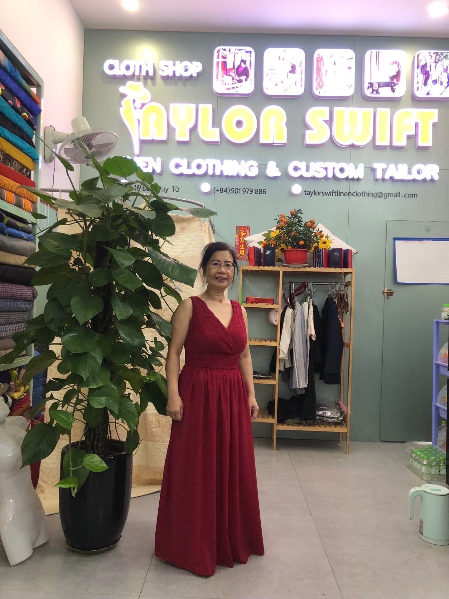 Woman in a red dress standing in front of "Taylor Swift Fine Clothing & Custom Tailor" shop.