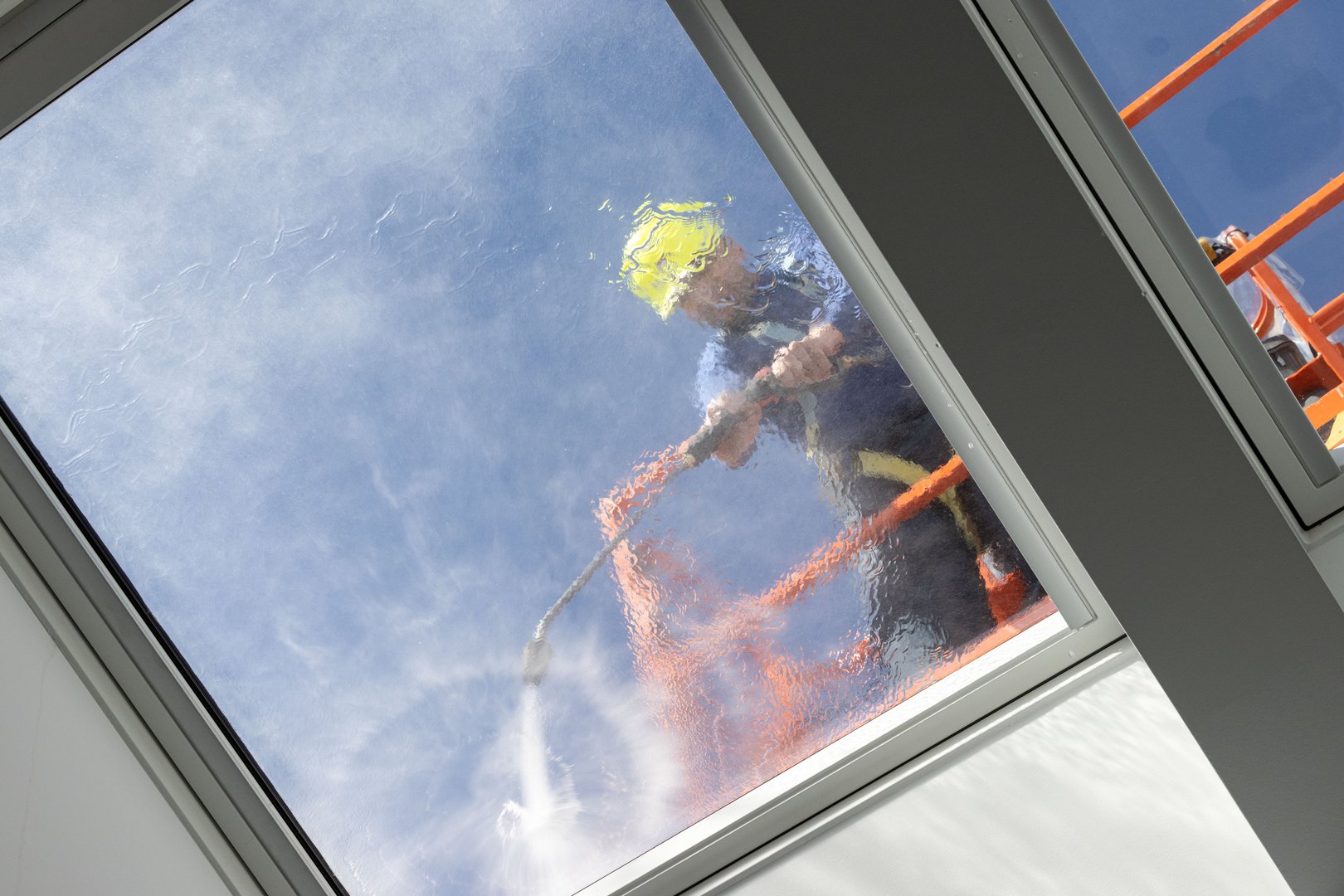 A Worker on a cherry picker cleaning a roof windows with high pressure water jet. Low angle shot
